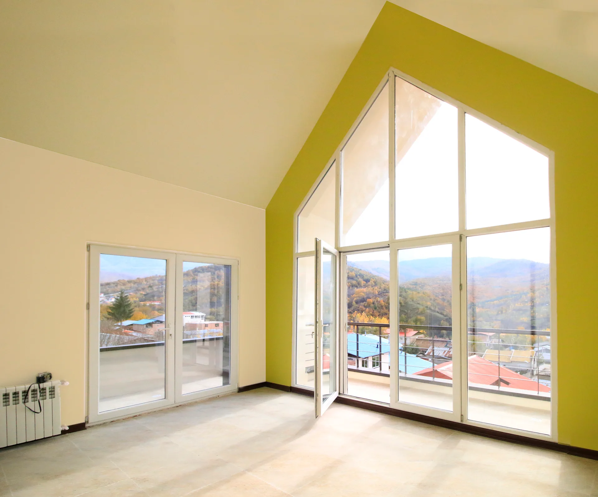 An empty room features a high vaulted ceiling, a mustard yellow accent wall around a large gabled window, and light tile flooring.