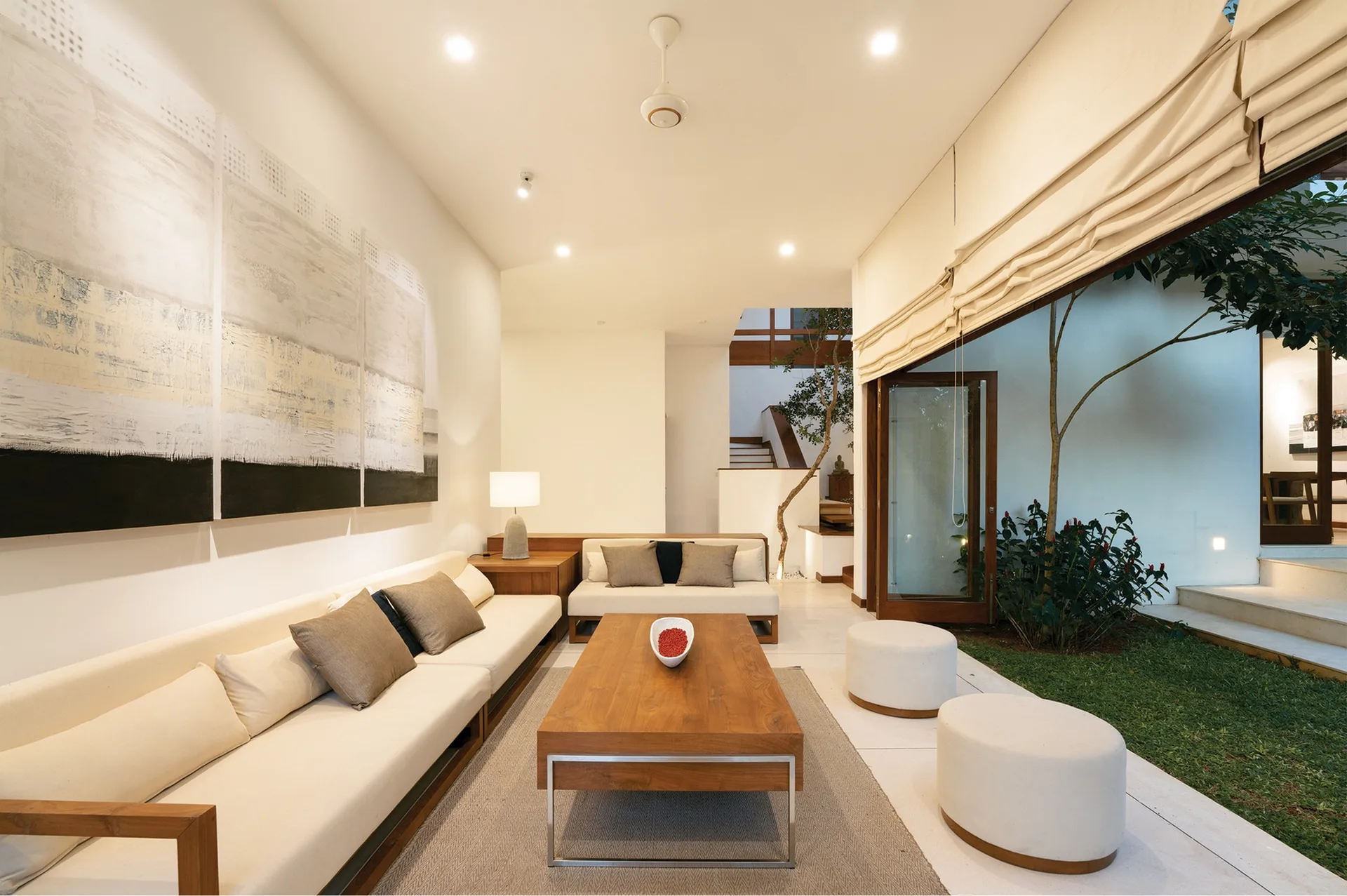 A modern living room features a low-profile wood sectional sofa, a matching coffee table, and large sliding doors that open to a green outdoor courtyard.