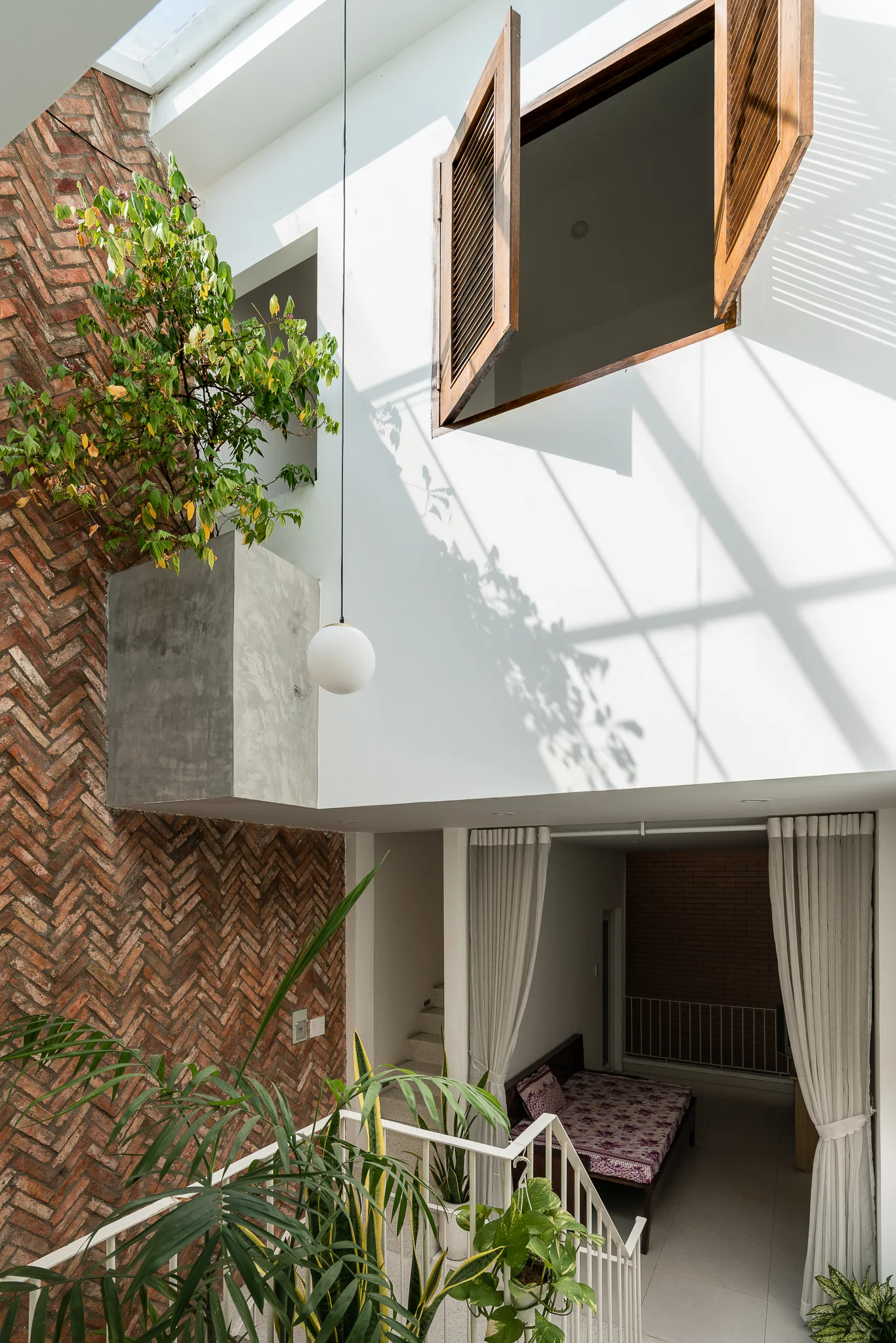 A multi-level interior atrium features a herringbone brick wall, a suspended concrete planter with greenery, and open wooden shutters on the upper floor.