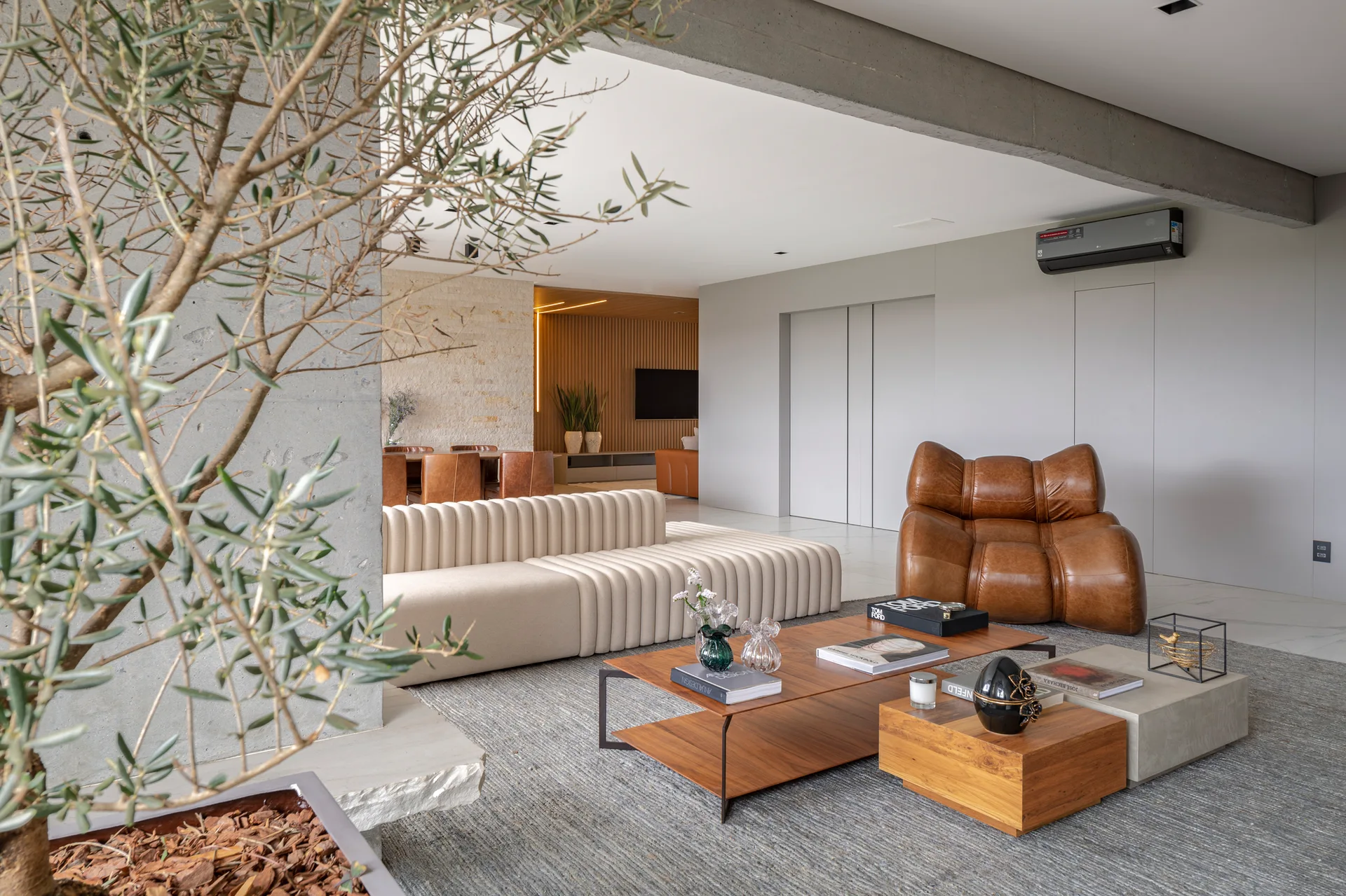 A contemporary living room featuring a cream-colored channeled sofa, a brown leather lounge chair, and tiered coffee tables on a grey rug.