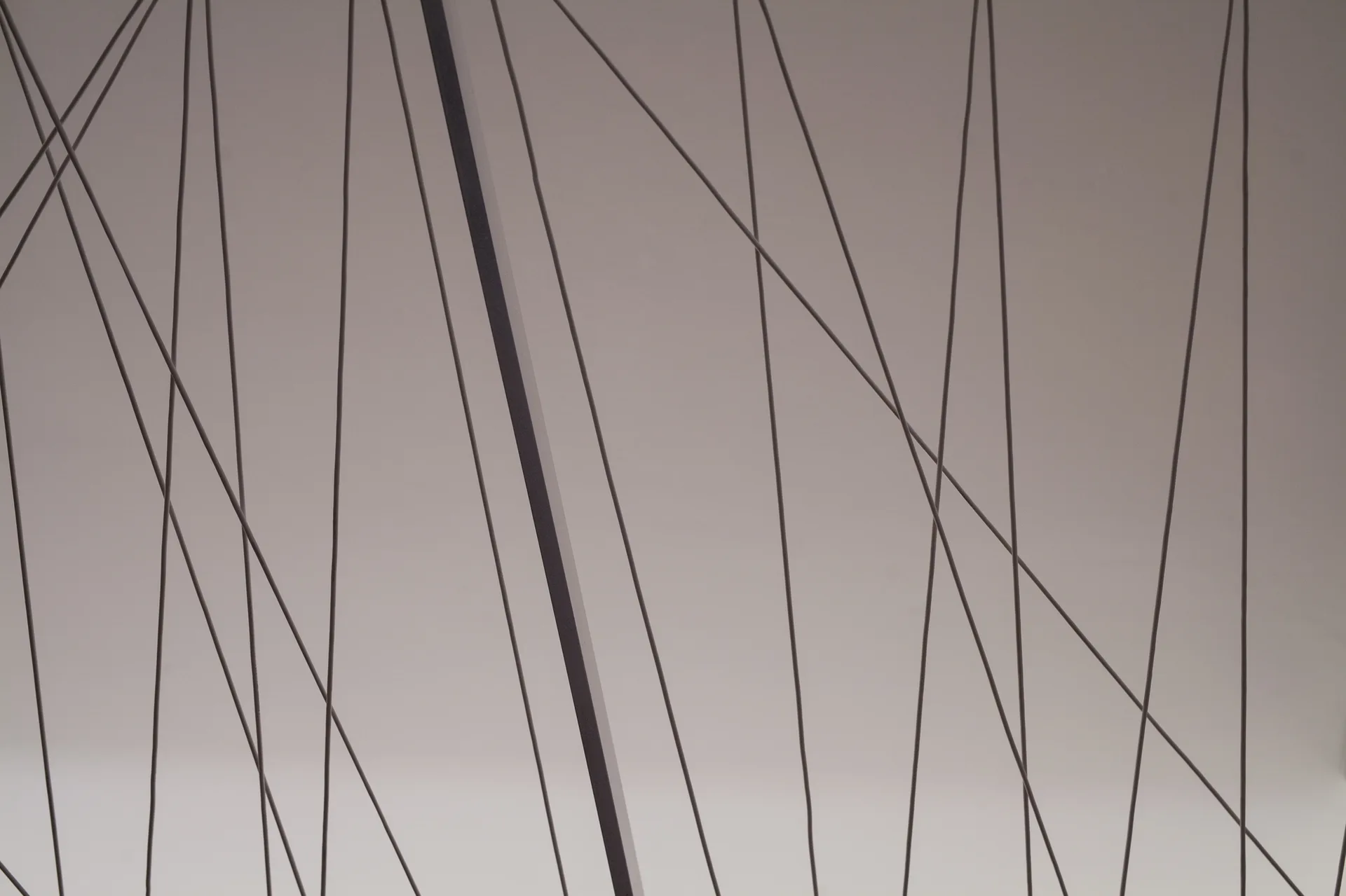 Thin dark metal tension cables cross diagonally in front of a smooth, matte light grey wall in a modern architectural detail.