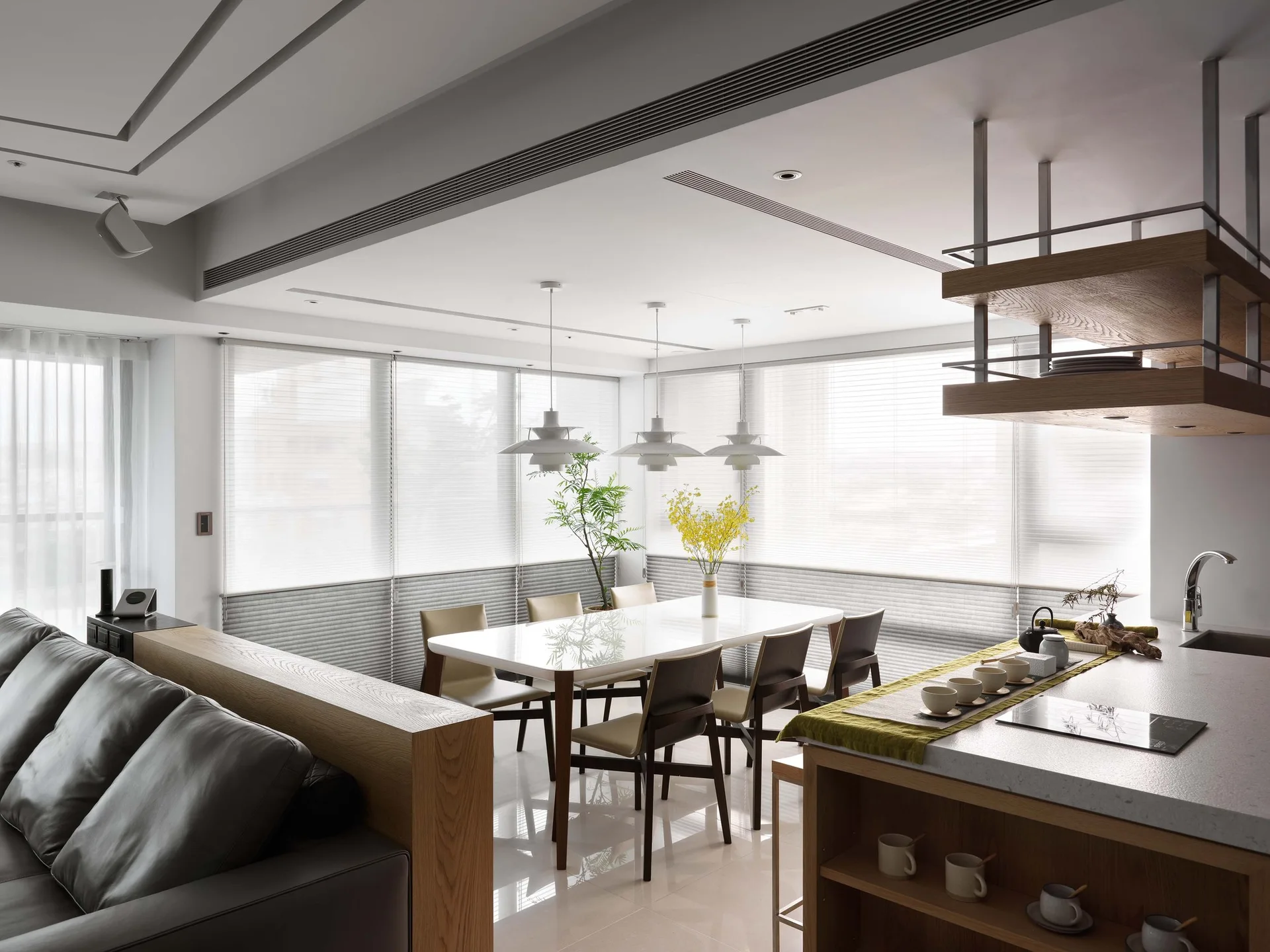 A modern open-plan dining area features a white table, three pendant lights, and a kitchen island with a hanging wooden shelf.