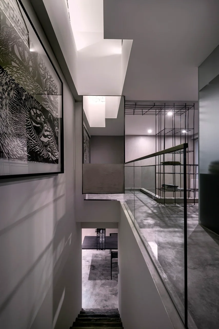 An industrial stair landing with concrete floors, a glass railing, a black metal grid shelf, and a large graphic framed print on a gray wall.