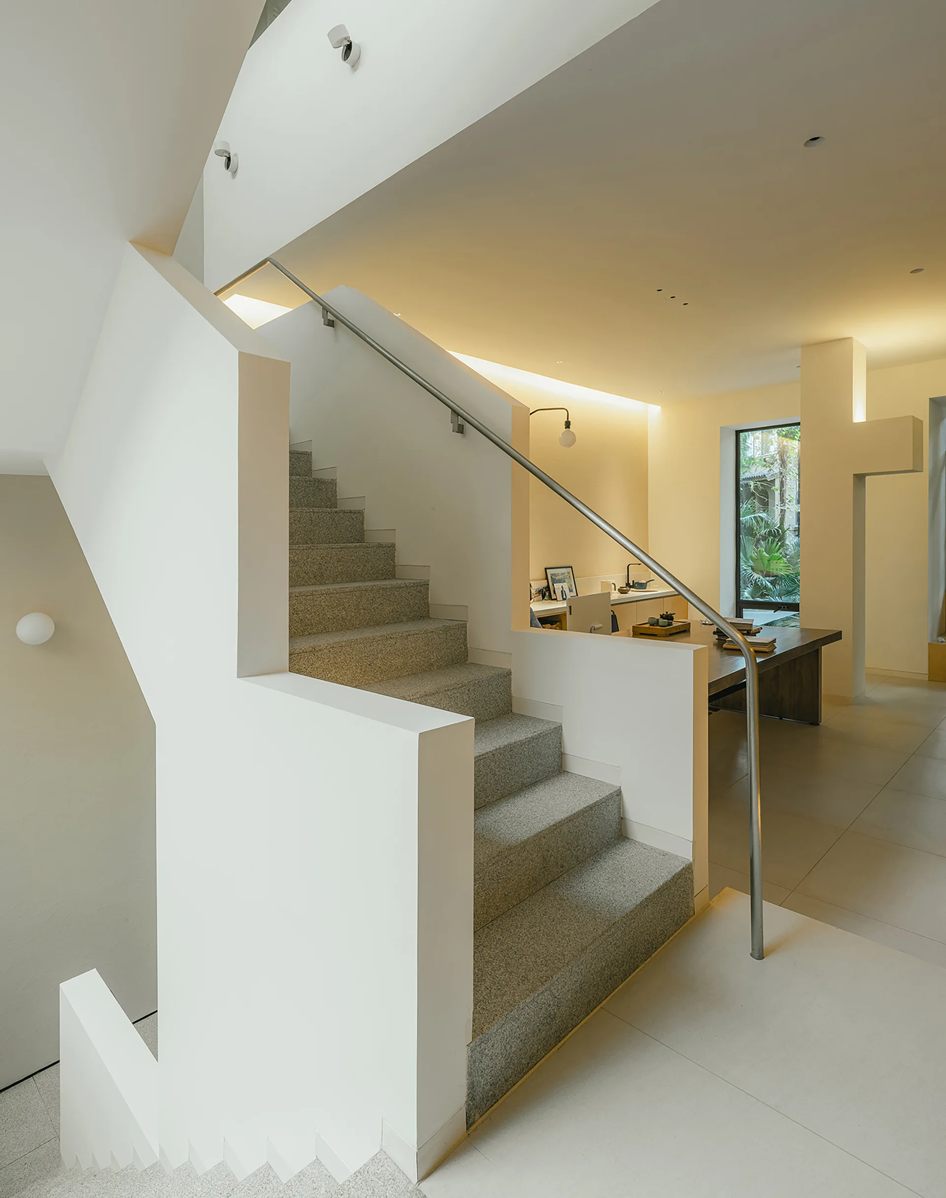 A minimalist staircase with textured grey stone treads and a solid white balustrade stands in a bright, modern open-plan home.