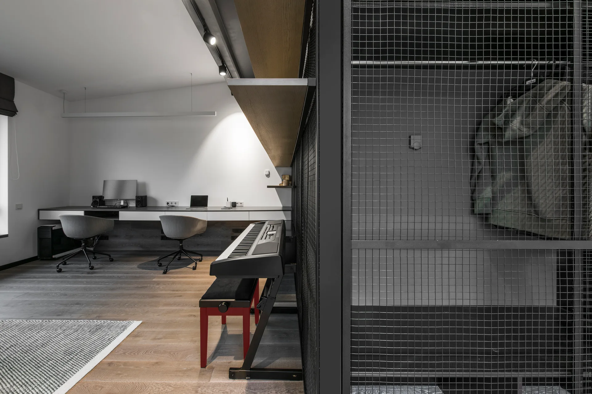 A modern home office features a long white desk with two gray chairs, a digital keyboard, and a tall black wire-mesh partition screen.