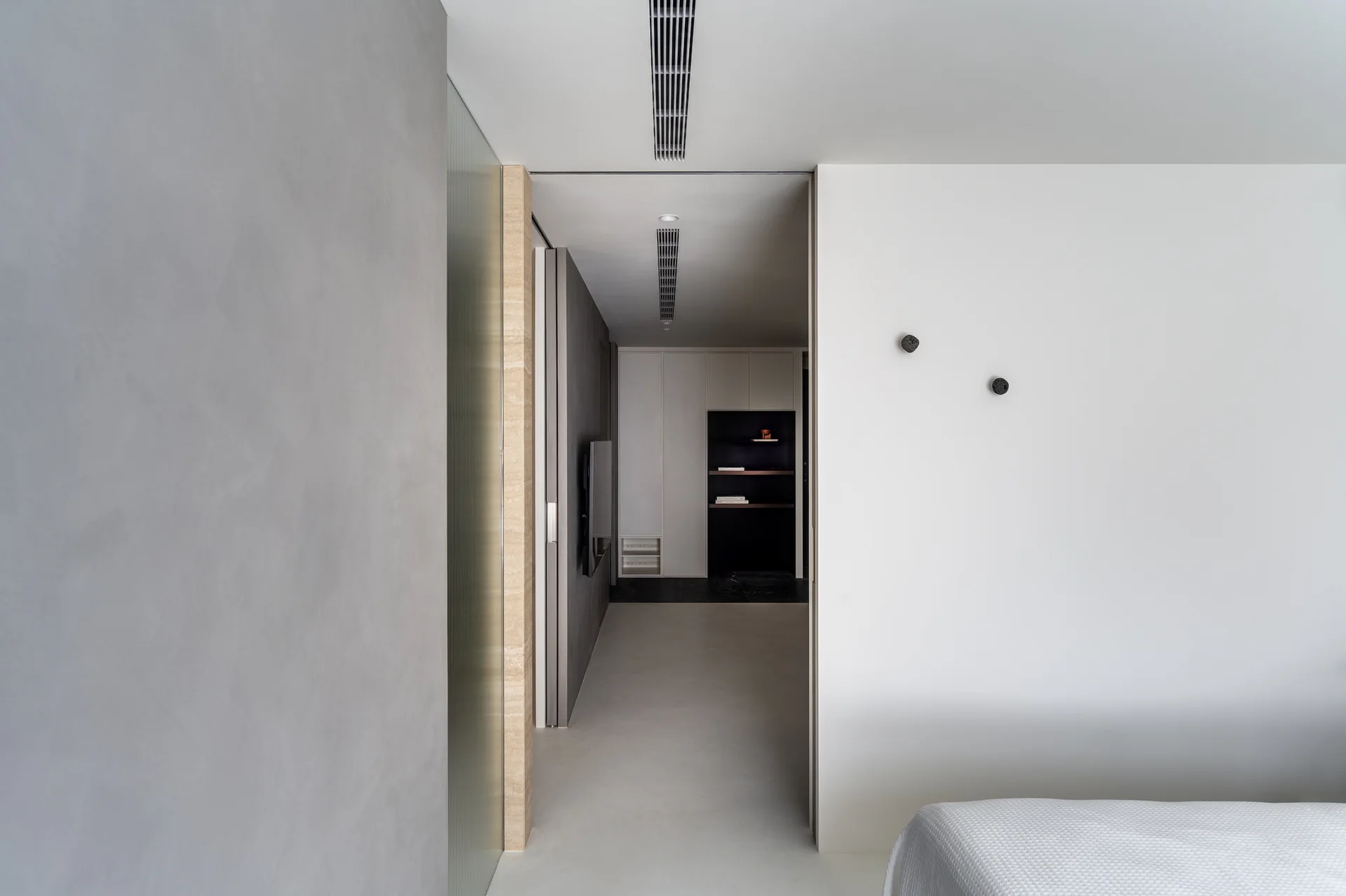 A minimalist hallway features textured light grey walls, a ribbed glass panel, black linear ceiling vents, and built-in storage cabinets.