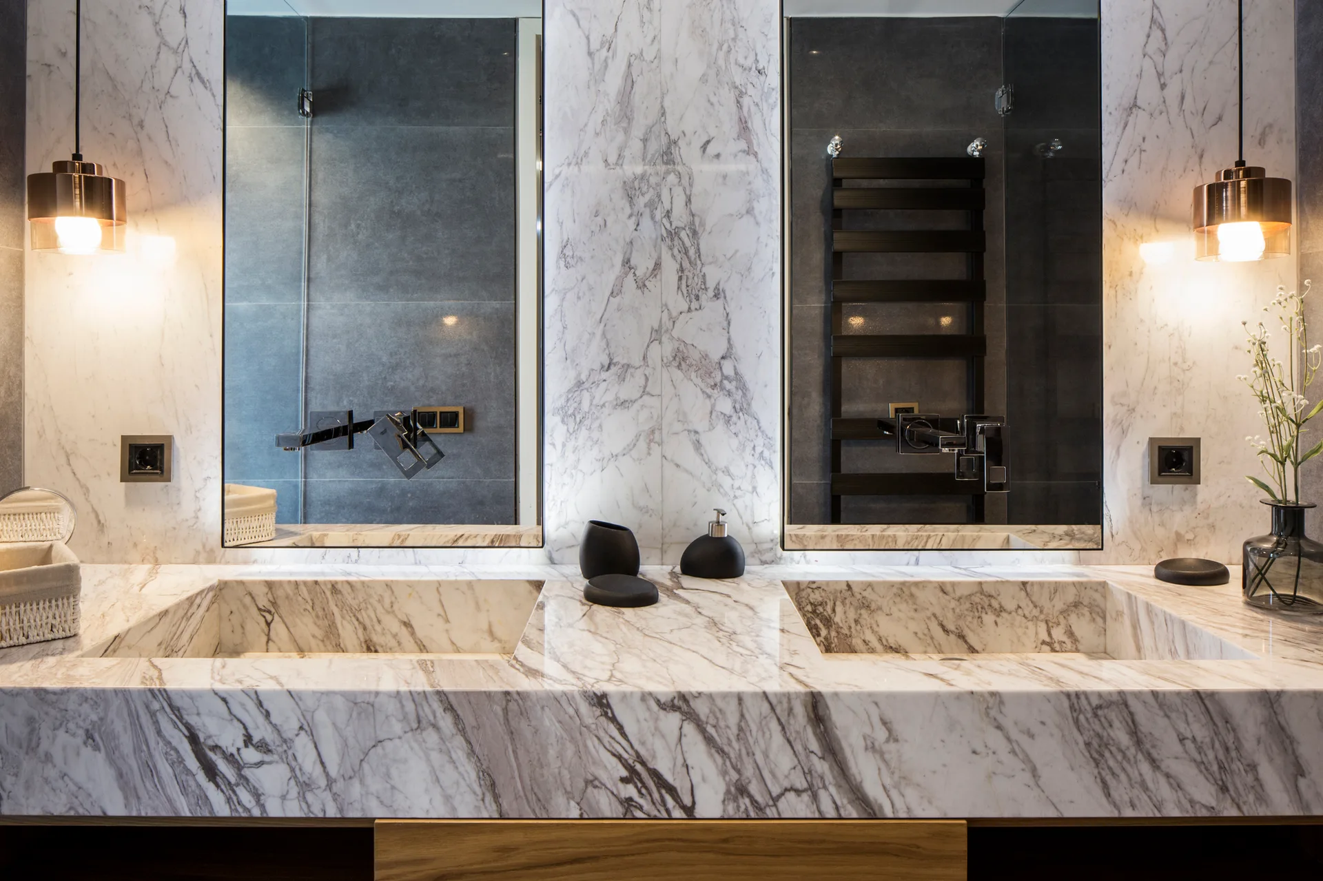 A contemporary bathroom features a veined marble vanity with integrated double sinks, tall rectangular mirrors, and hanging copper pendant lights.