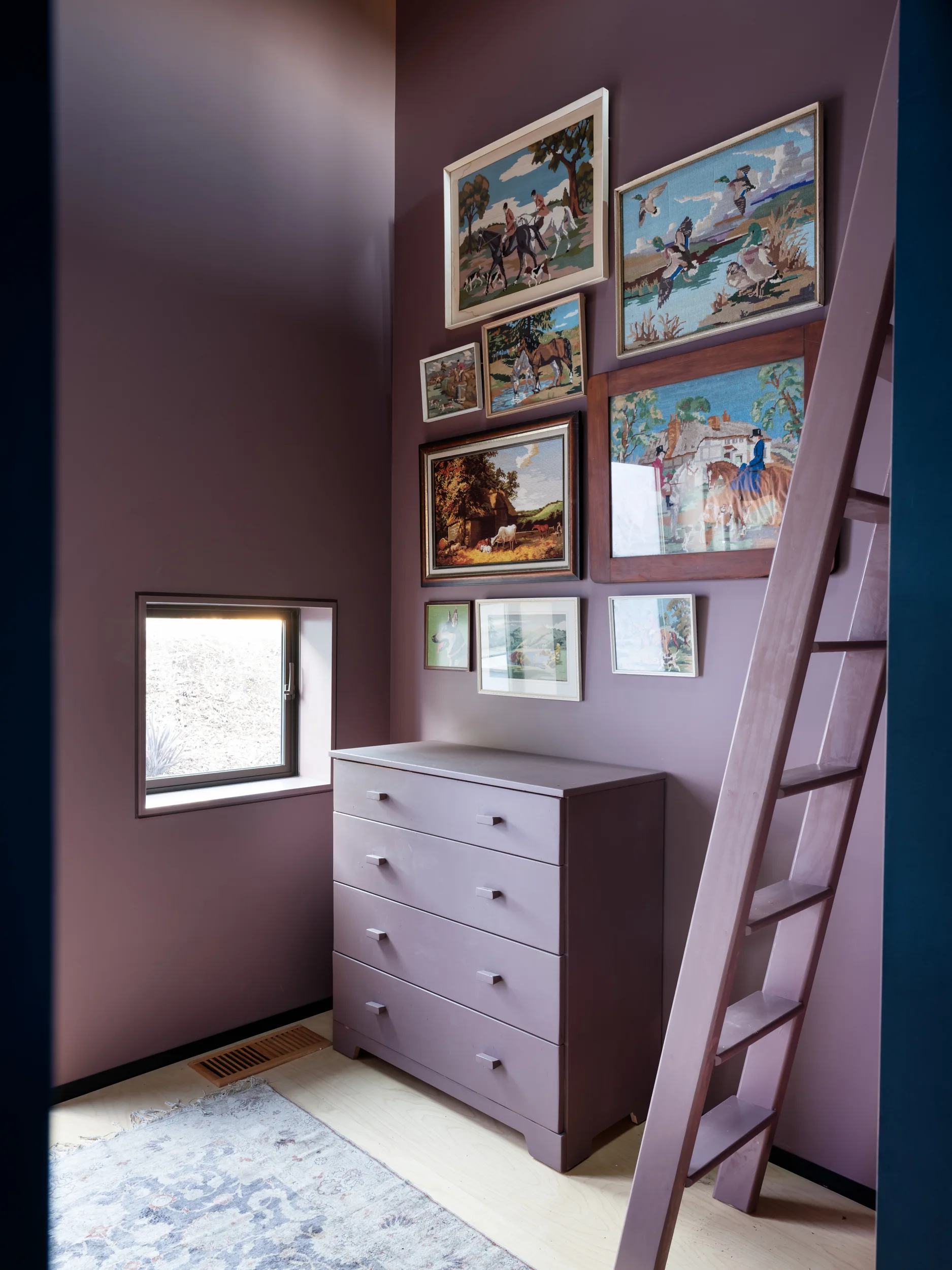A room corner features mauve walls, a matching chest of drawers, a leaning wooden ladder, and a gallery wall of framed vintage needlepoint art.