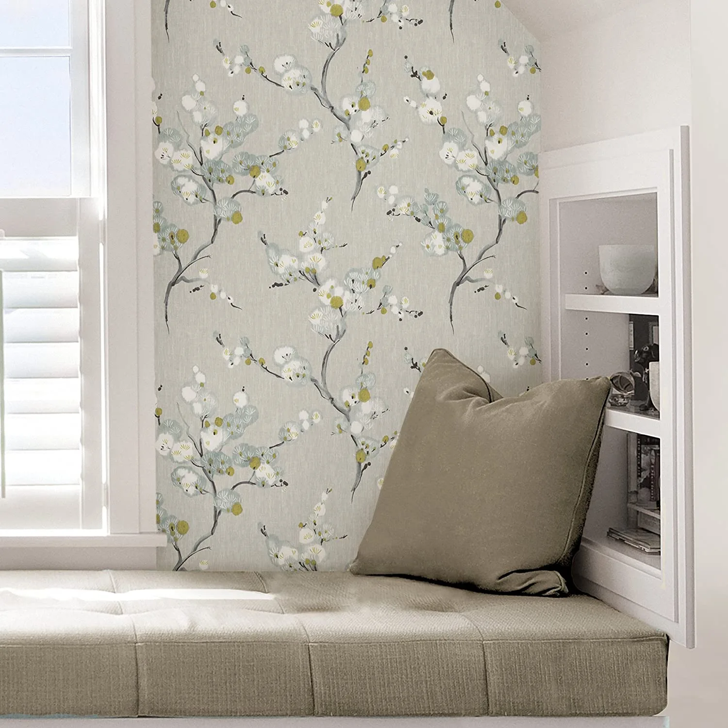 A tufted window seat is paired with a floral branch wallpaper, a brown accent pillow, and a white built-in shelving unit.
