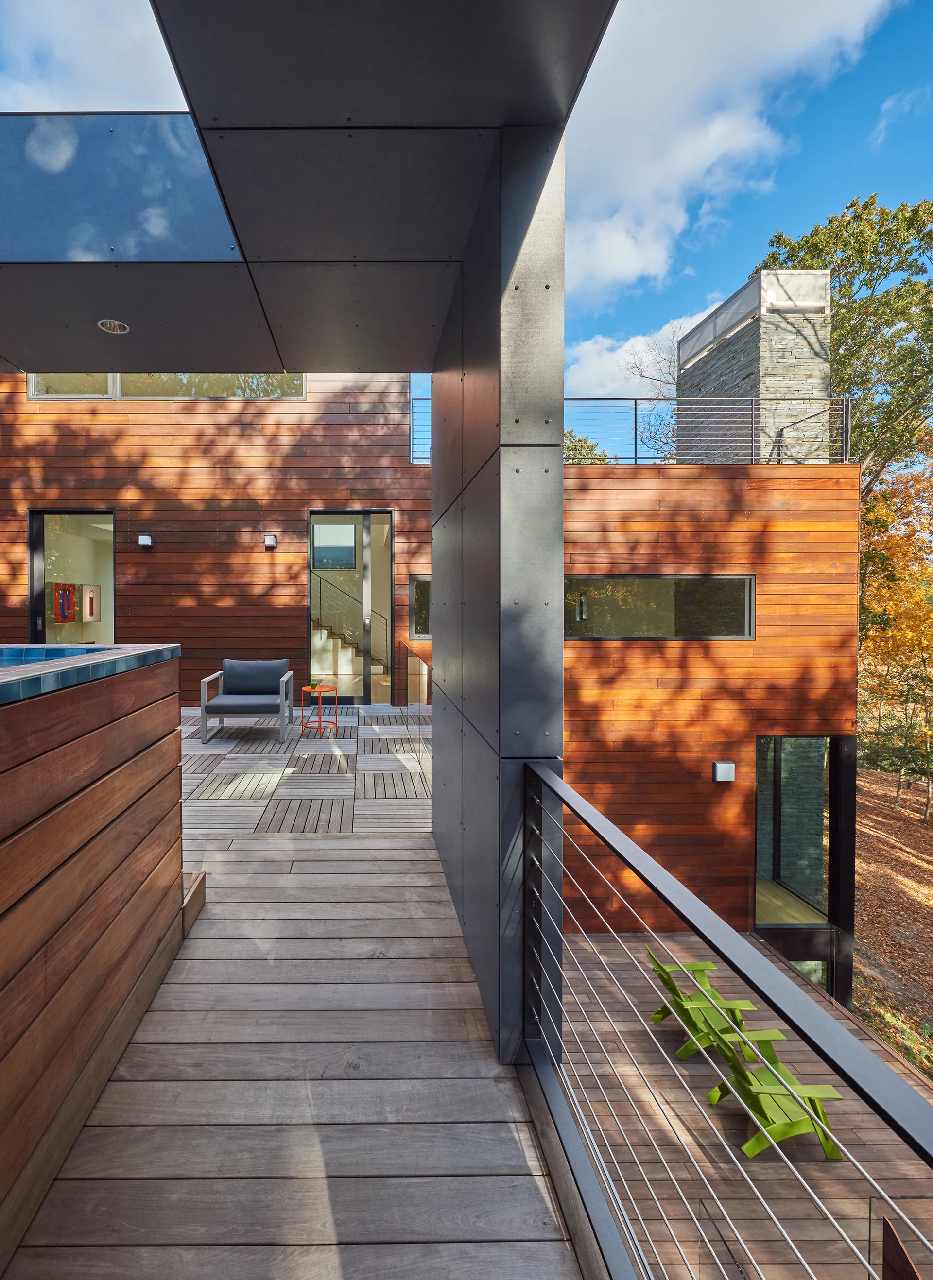 A modern multi-level wood deck features warm cedar siding, a dark metal architectural support column, and horizontal cable railings.