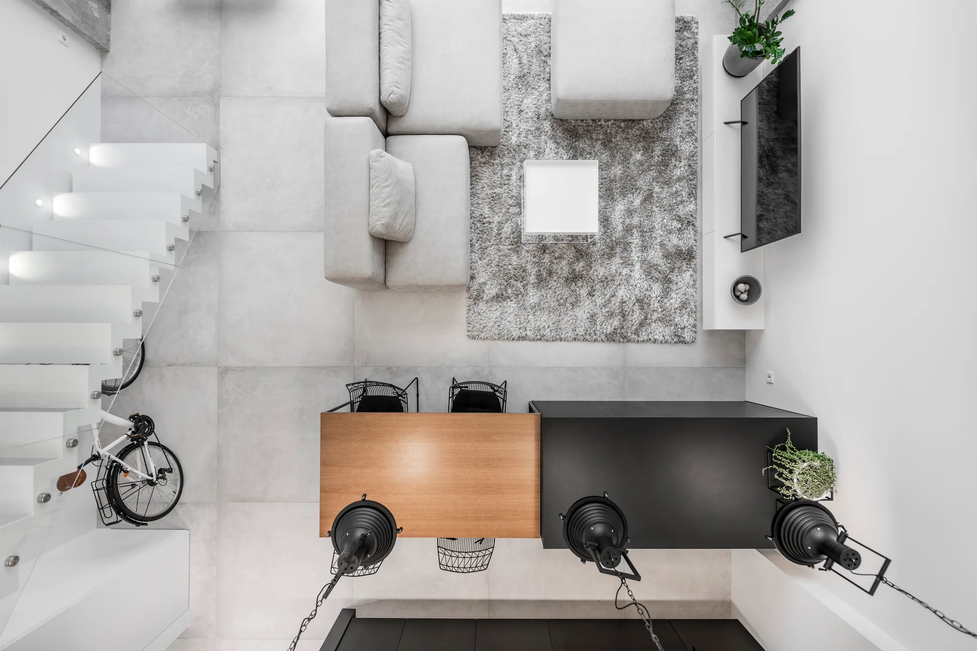 A top-down view of a modern open-plan space featuring a light grey sectional sofa on a shaggy rug next to a wood and black dining table.
