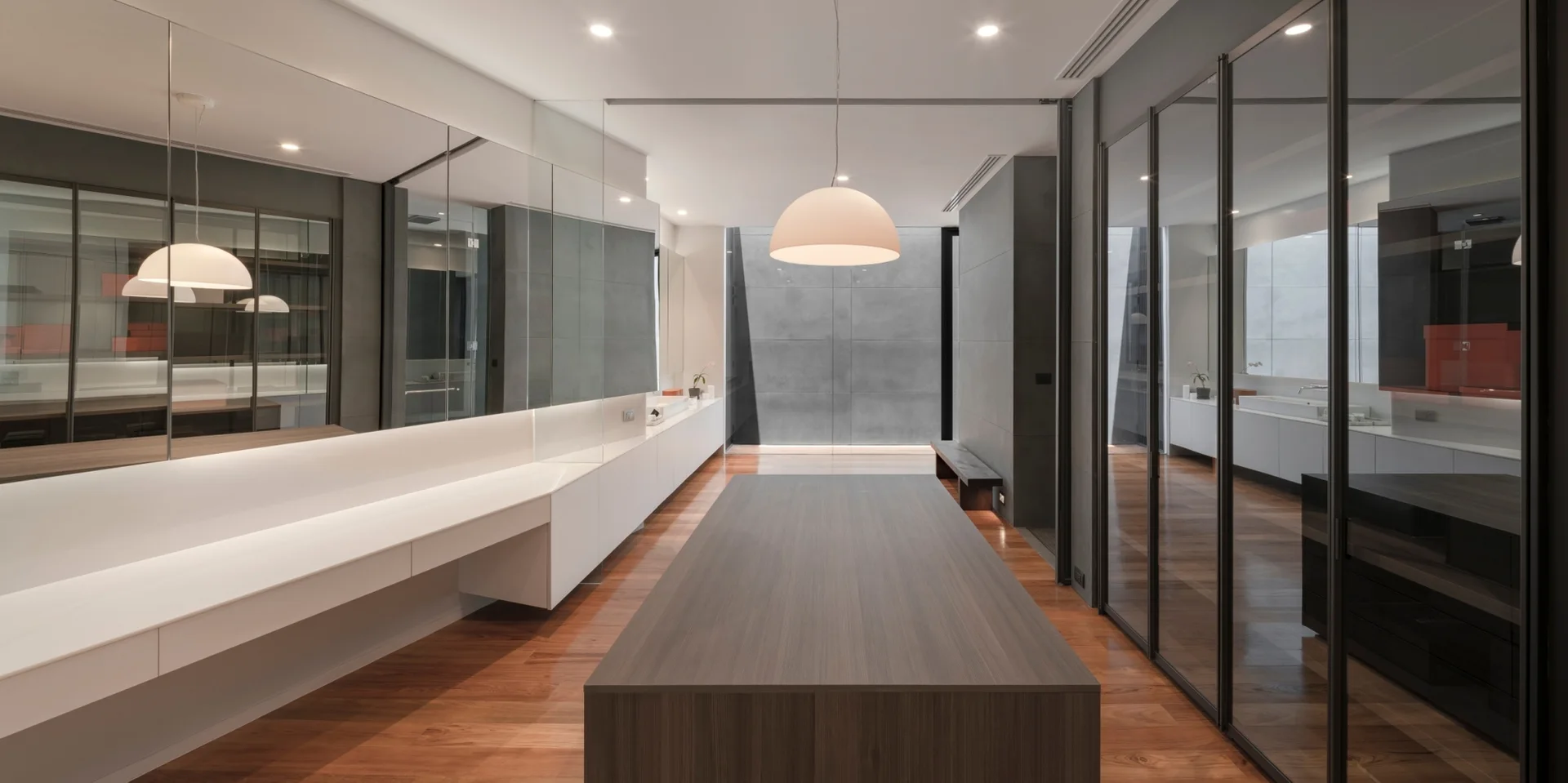 A spacious dressing room featuring a central wood-grain island, floor-to-ceiling mirrored walls, and glass-door wardrobes.