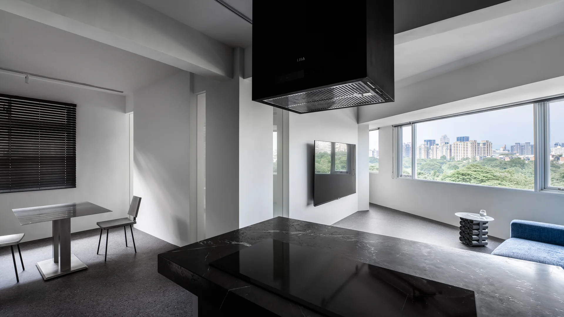 A modern open-plan kitchen features a large black stone island with a matching range hood, a dining area, and dark slate flooring.