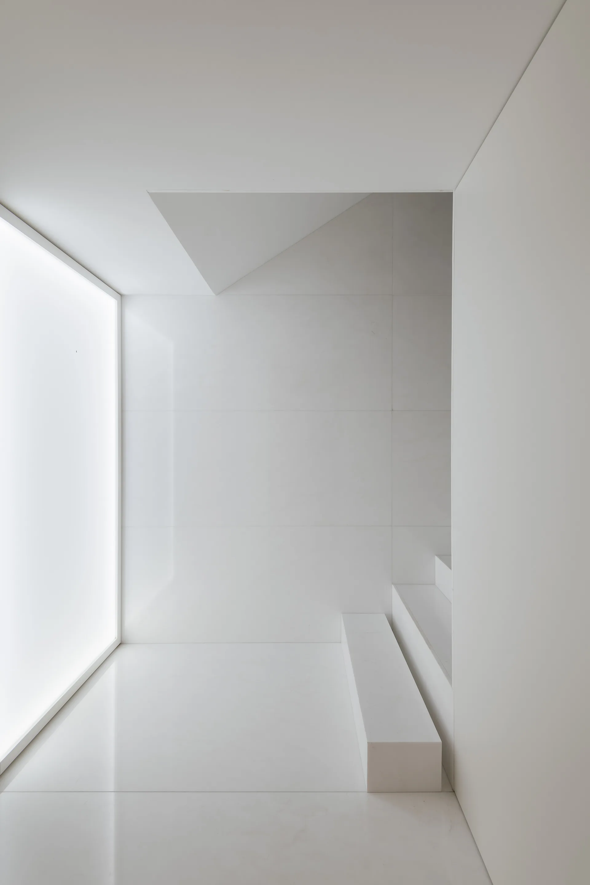 A minimalist monochromatic white staircase area featuring clean stone-like steps next to a large rectangular backlit wall panel.