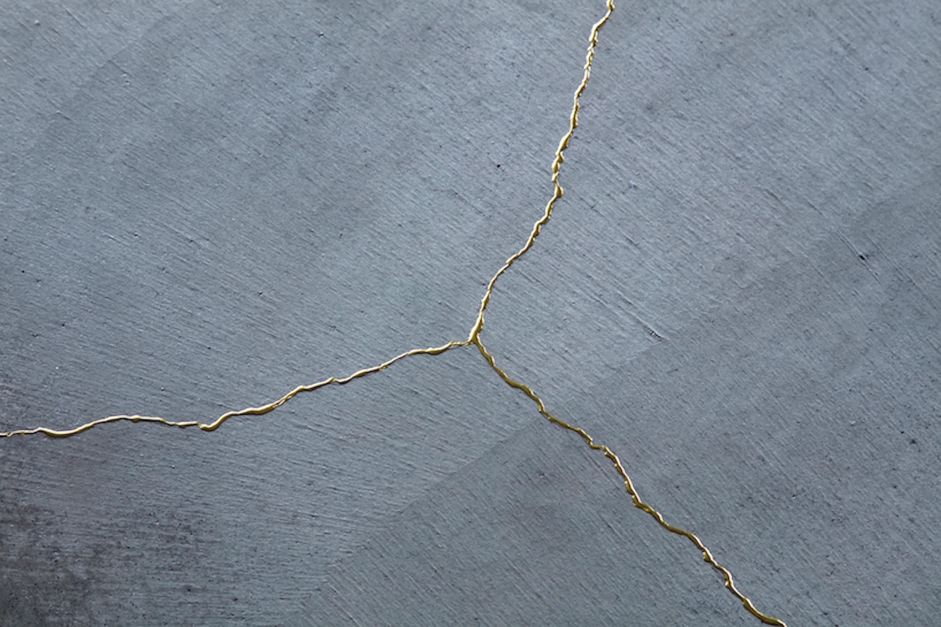 A close-up of a matte grey textured surface with a branching, decorative gold-filled crack detail in the style of Japanese kintsugi.
