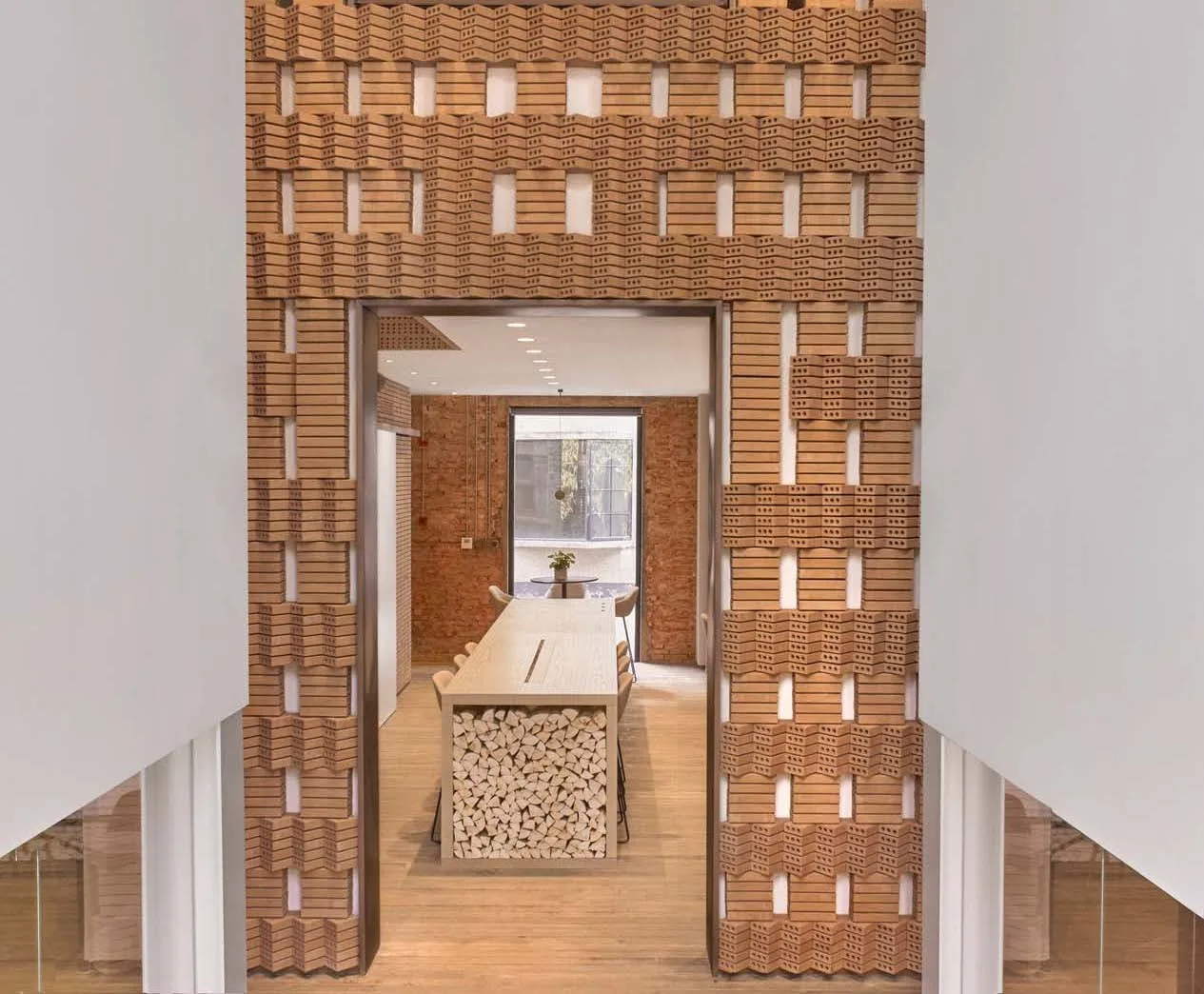 A dining room with a long wood table is viewed through an intricate, geometric terracotta brick entryway.