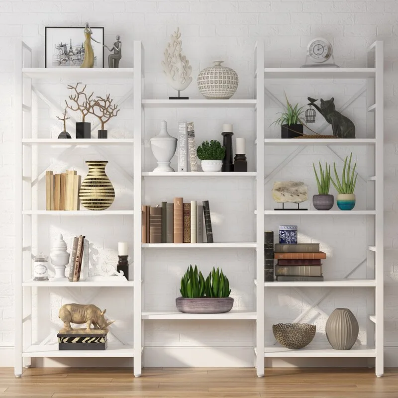 A three-section white open metal shelving unit styled with books, ceramic vases, and small green plants stands against a white painted brick wall.