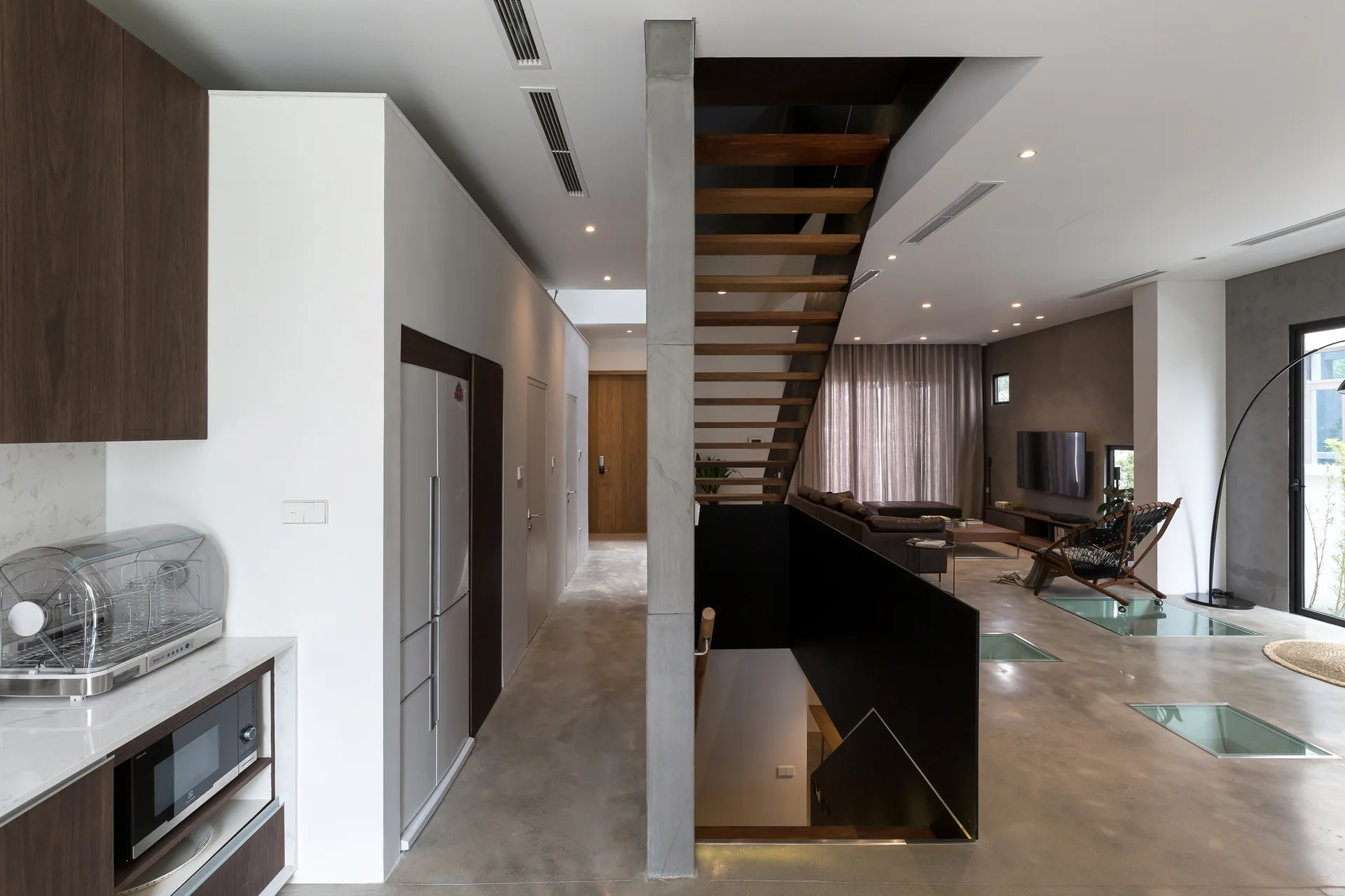 A modern open-plan home featuring a central floating staircase, polished concrete floors with inset glass panels, and a living area.