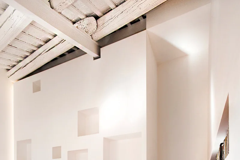 A clean white wall with several square recessed niches beneath an exposed wood plank and steel beam ceiling.