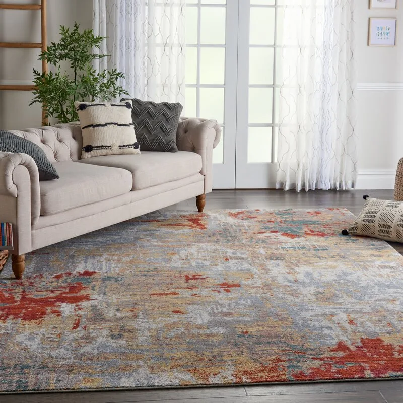 A tufted light beige sofa sits on a large distressed area rug with red and blue patterns in a sunlit living room.