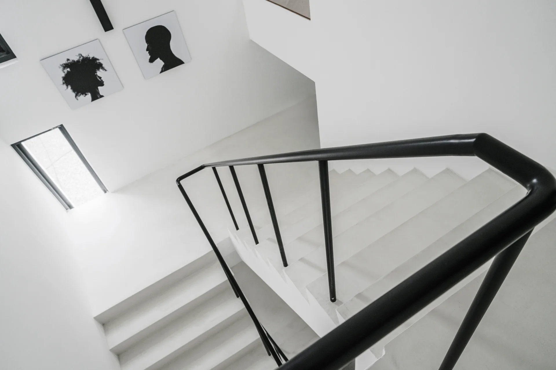 A minimalist white staircase features a continuous matte black handrail and two square black-and-white portrait prints on the landing wall.