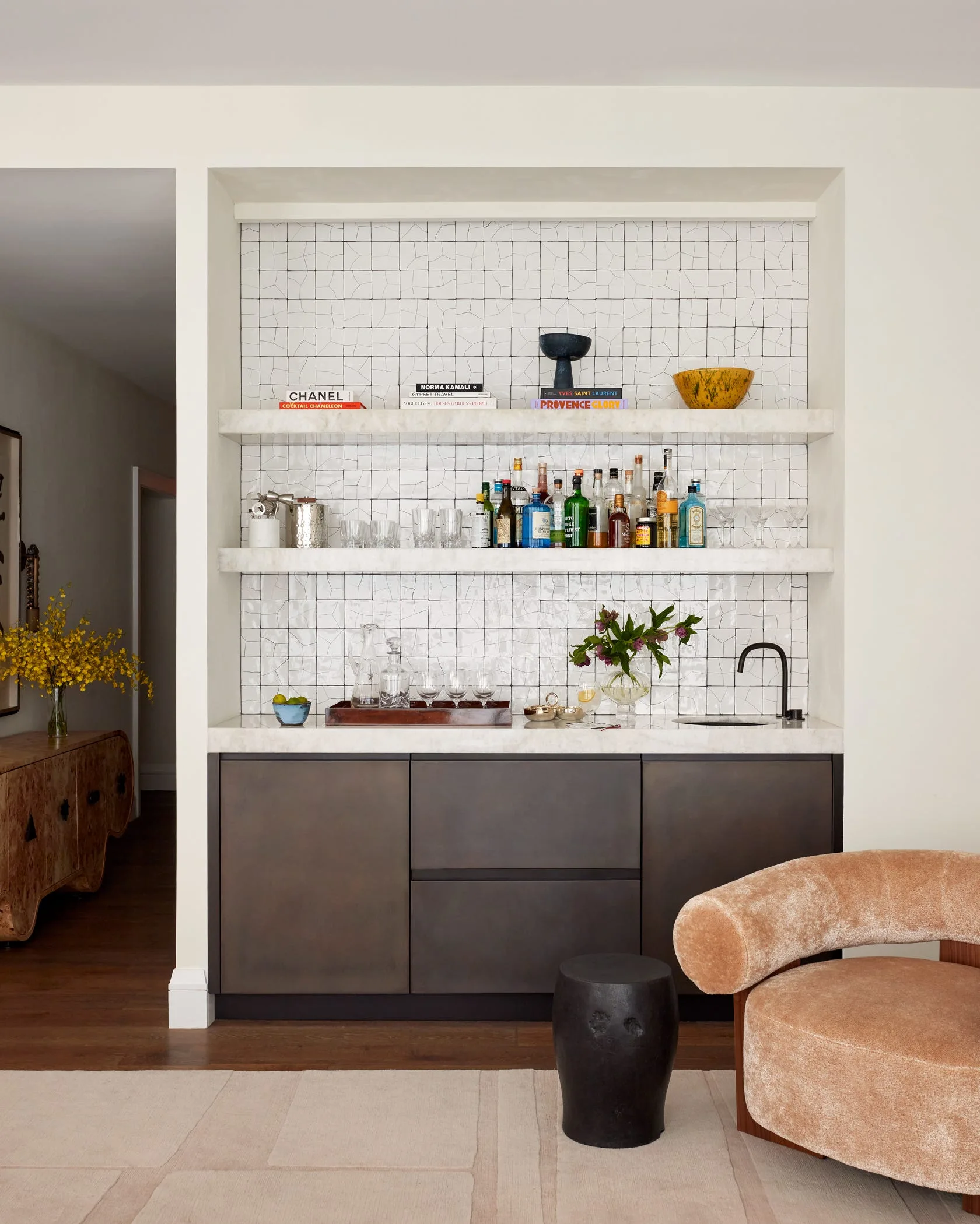 A built-in home wet bar featuring dark bronze lower cabinets, thick white marble shelves, and a white grid-patterned tile backsplash.