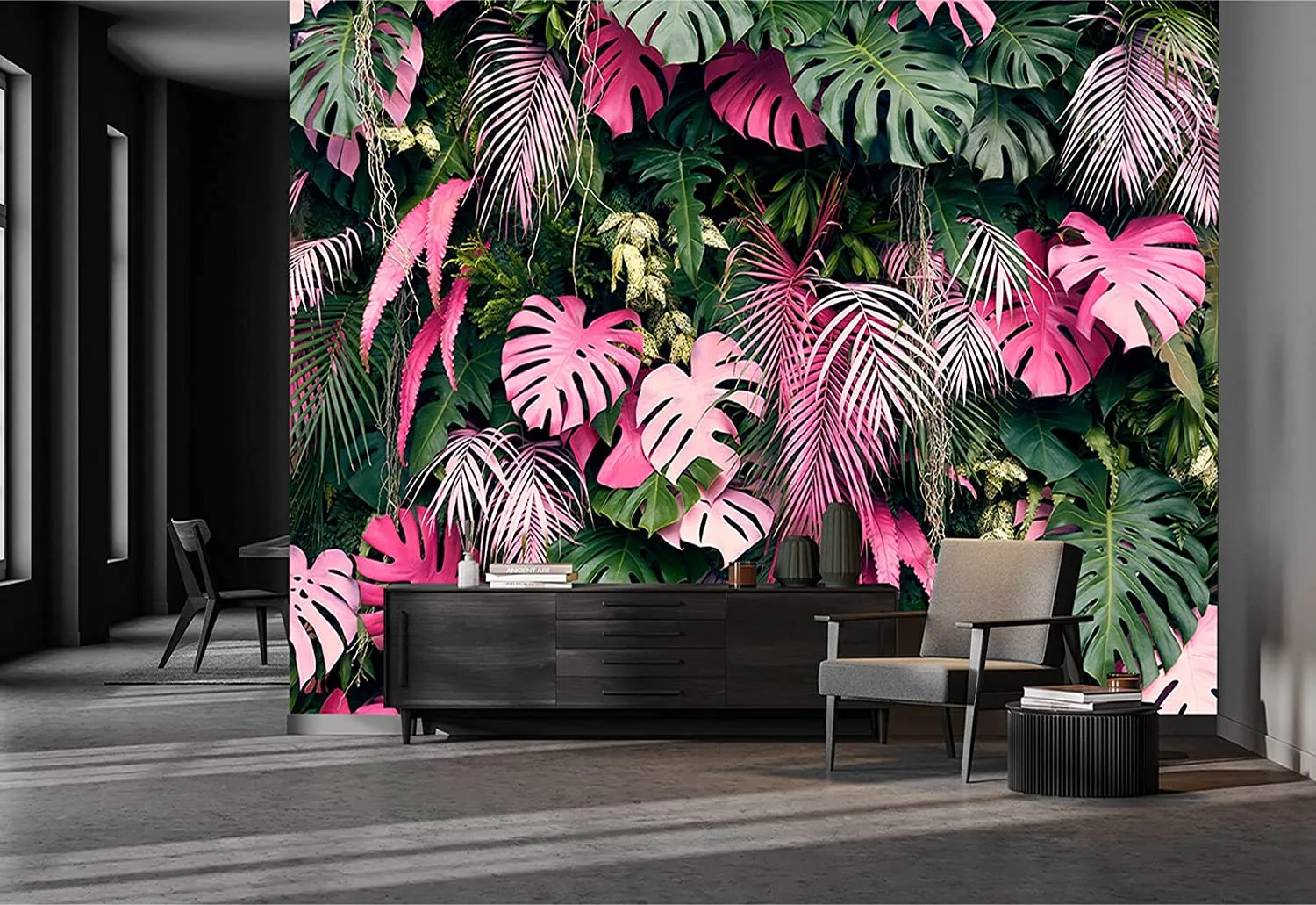 A modern living space features a bold pink and green tropical leaf wallpaper behind a black sideboard, a gray armchair, and a concrete floor.