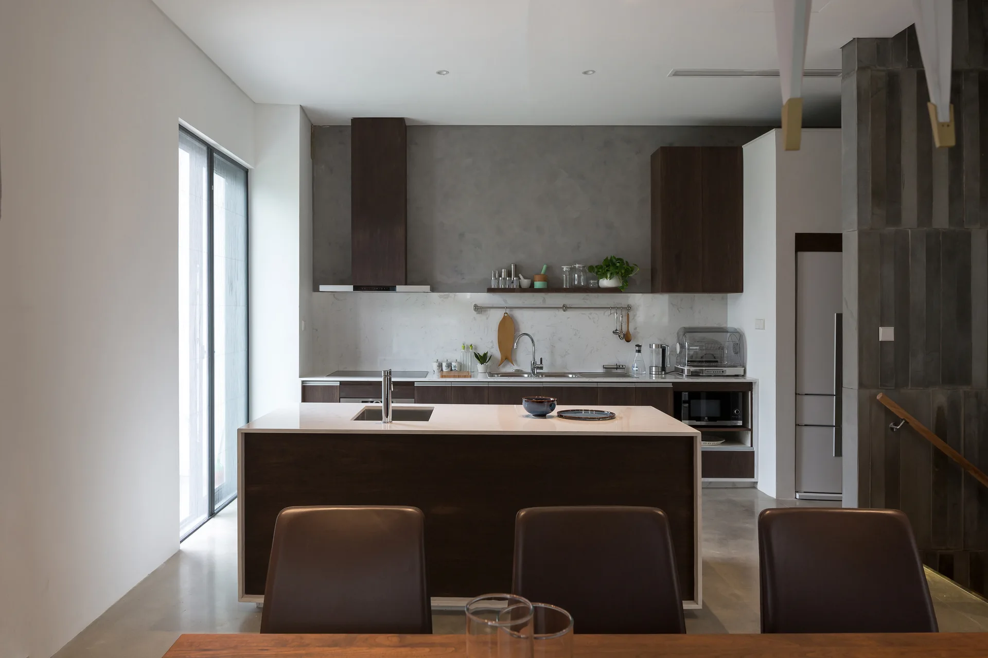 A modern kitchen featuring a dark wood island, matching cabinetry, a textured gray wall, and a white marble-veined backsplash.
