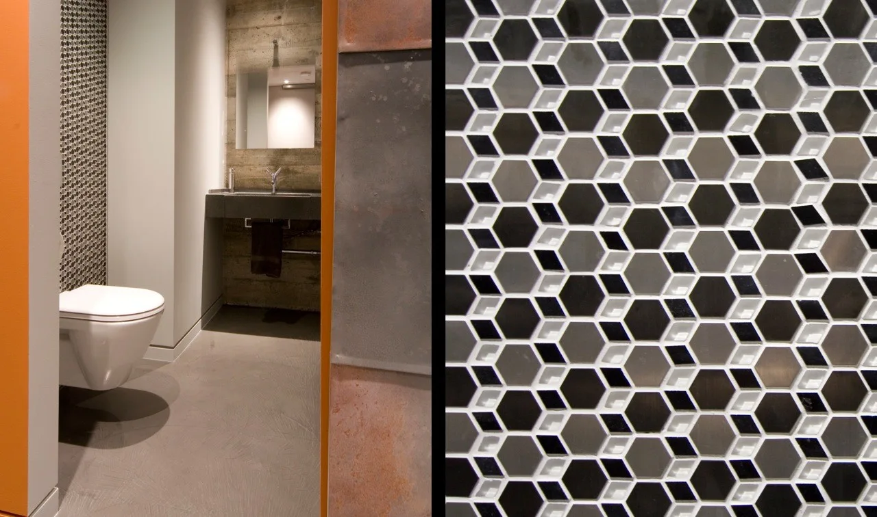 A modern bathroom features a wall-mounted toilet, concrete walls, and a detailed close-up of black, white, and metallic hexagonal mosaic tiles.