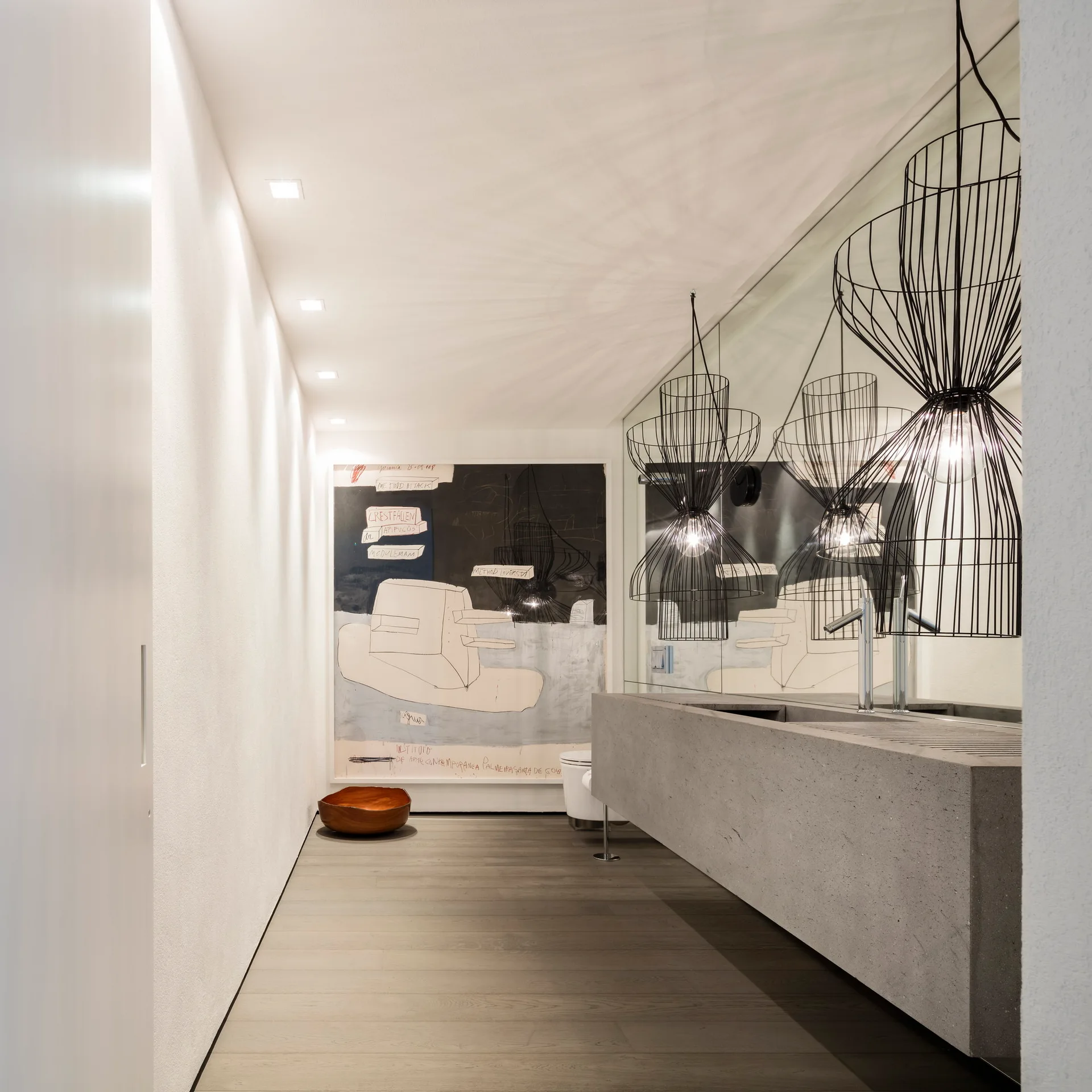 A minimalist bathroom featuring a wall-mounted grey concrete vanity, large mirror, and black wire geometric pendant lights.