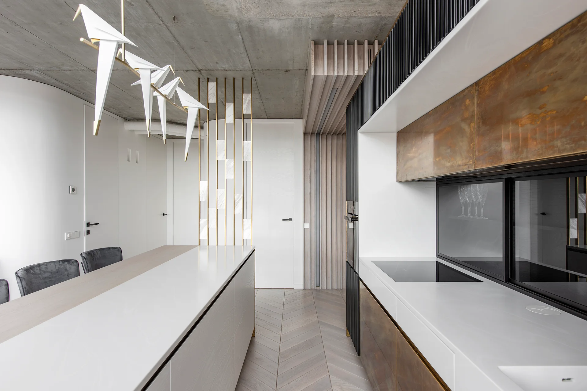 A modern kitchen features a white island, metallic bronze cabinets, an exposed concrete ceiling, and bird-shaped pendant lights.