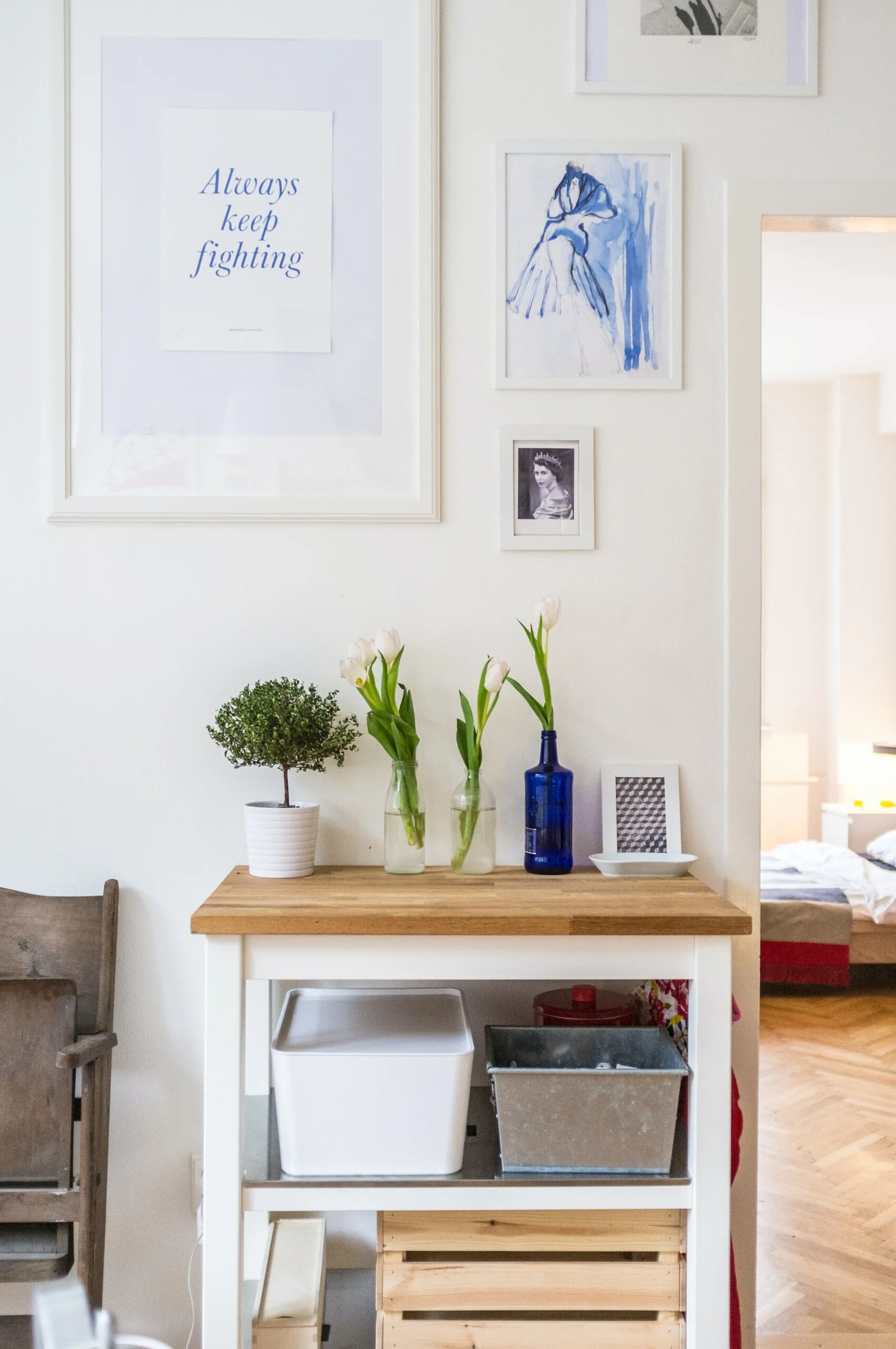 A white console table with a wooden top is styled with three flower vases and a small topiary beneath a gallery wall of framed art.