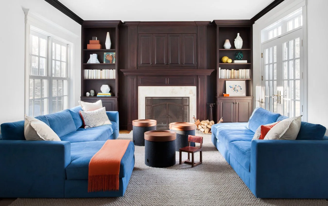 Two vibrant blue sofas face each other in a symmetrical living room featuring a central dark wood fireplace surround and built-in shelving.