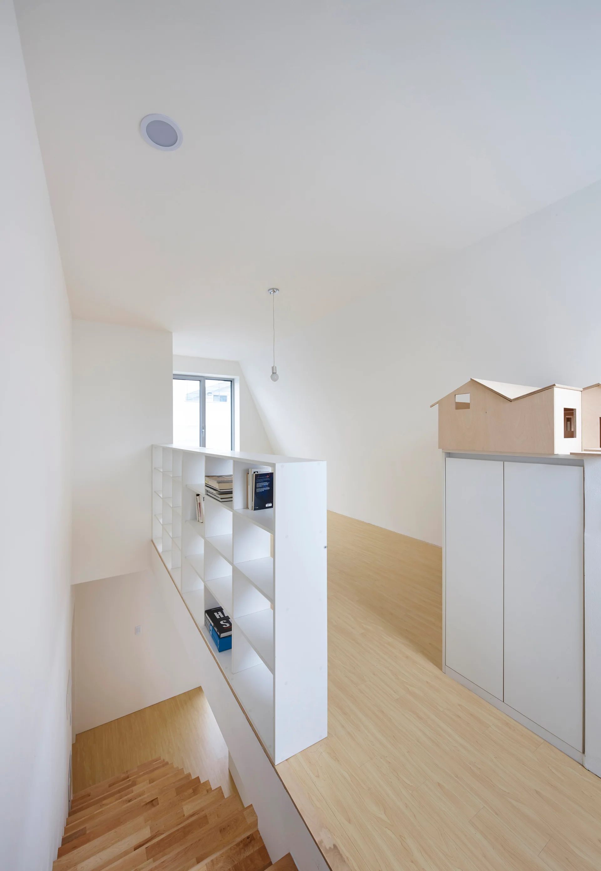 A bright lofted landing features light wood flooring, a white grid bookshelf acting as a guardrail, and a staircase leading up.