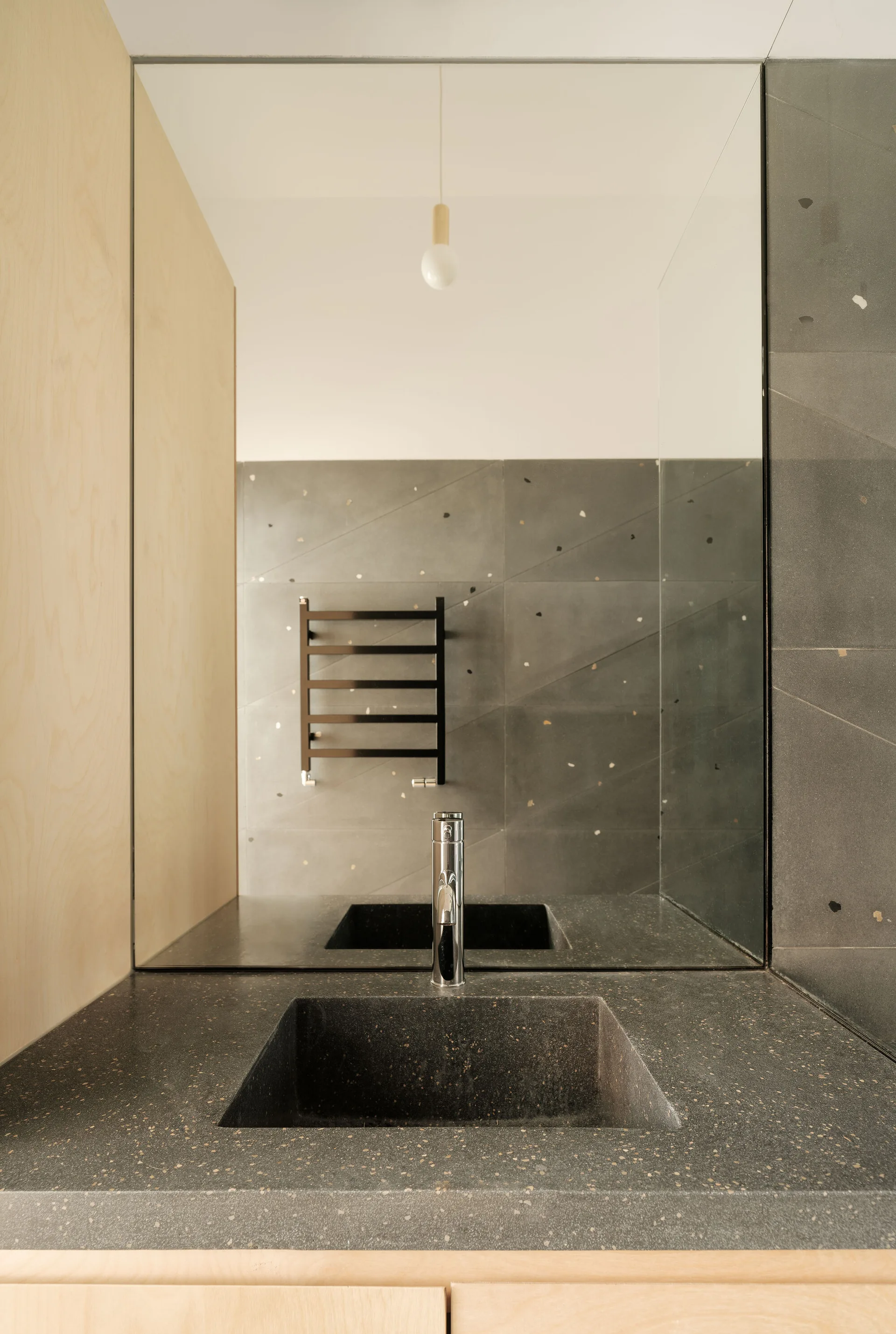A modern bathroom vanity featuring a dark speckled stone countertop with an integrated basin, light wood panels, and a large mirror.