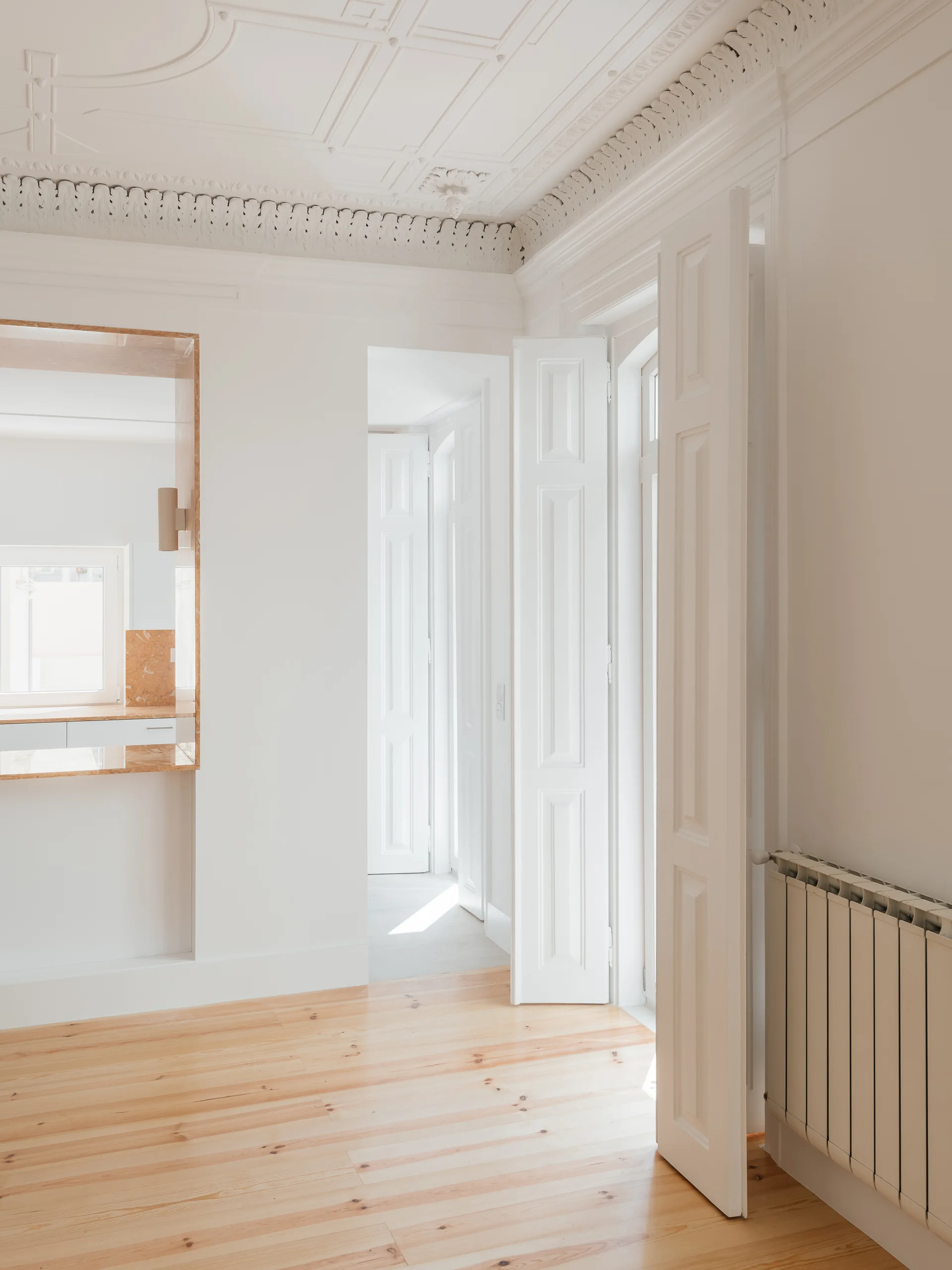 A bright hallway featuring light wood plank flooring, tall white paneled doors, and highly ornate classical plaster ceiling moldings.