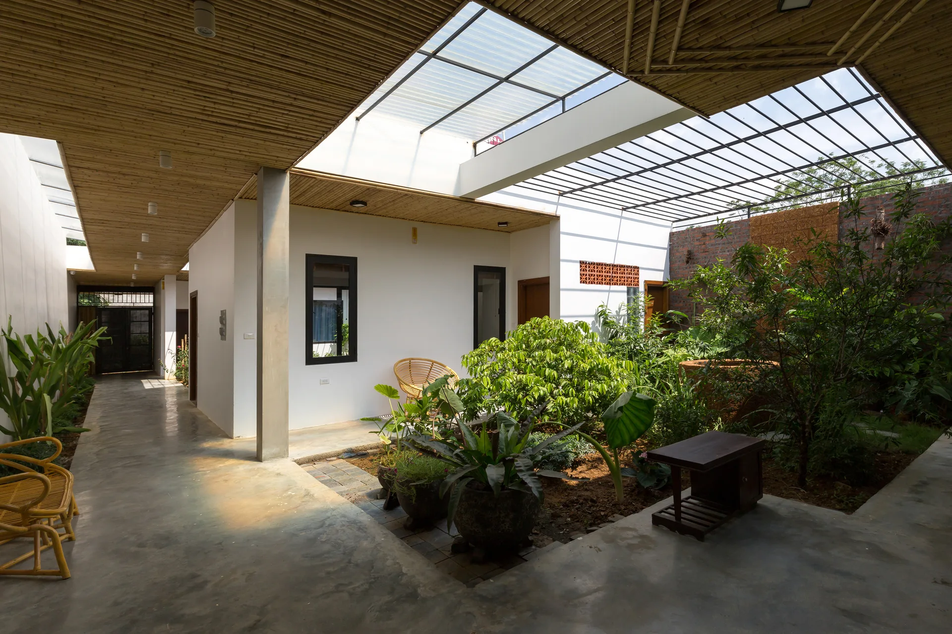 A semi-outdoor courtyard featuring a polished concrete floor, a bamboo-slatted ceiling with skylights, and a lush green central garden.