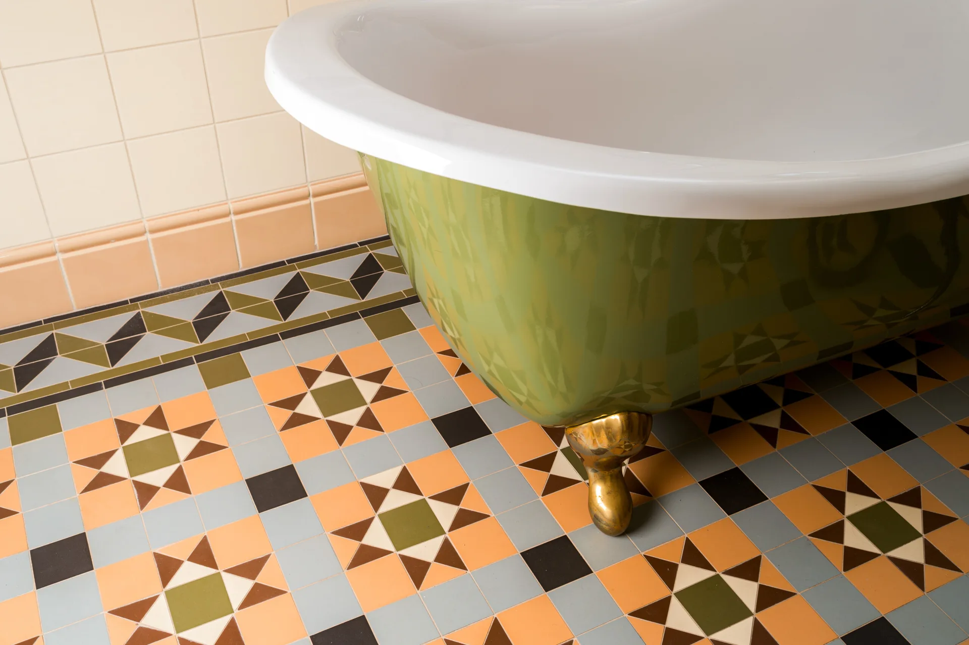 A green clawfoot bathtub with brass feet rests on a bathroom floor tiled in a colorful geometric star pattern.