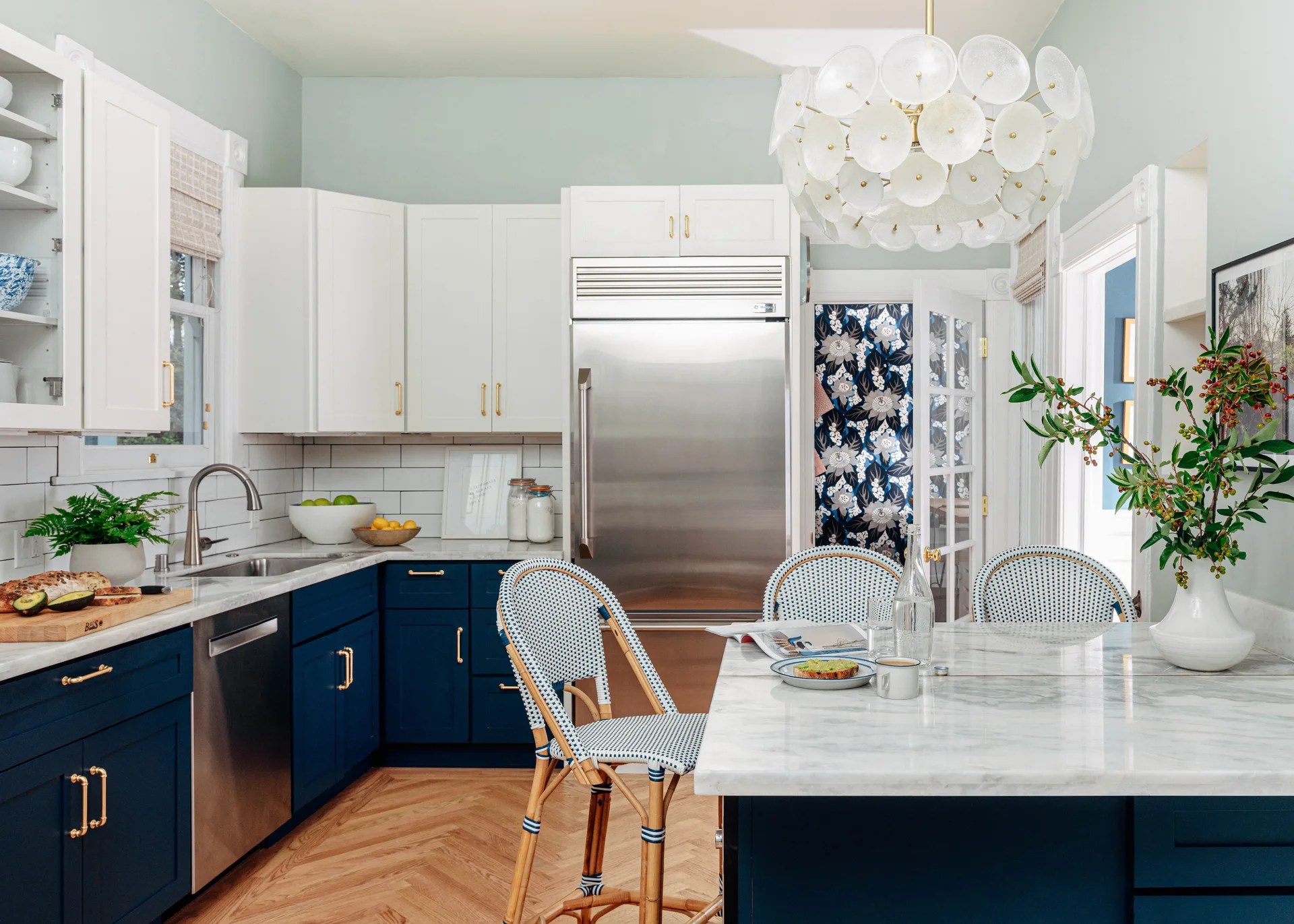 Kitchen with navy lower cabinets, white upper cabinets, a marble-topped island with woven bistro stools, and a circular glass chandelier.