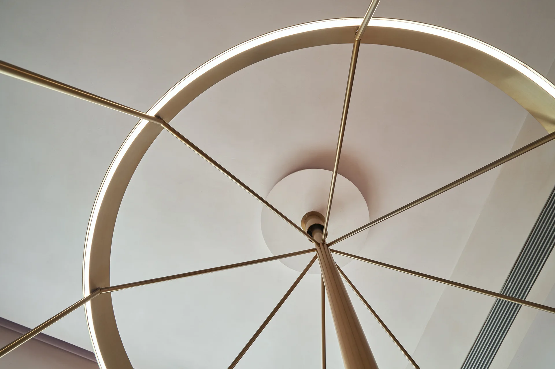 A low-angle view of a circular brass chandelier with integrated lighting mounted on a smooth white ceiling.