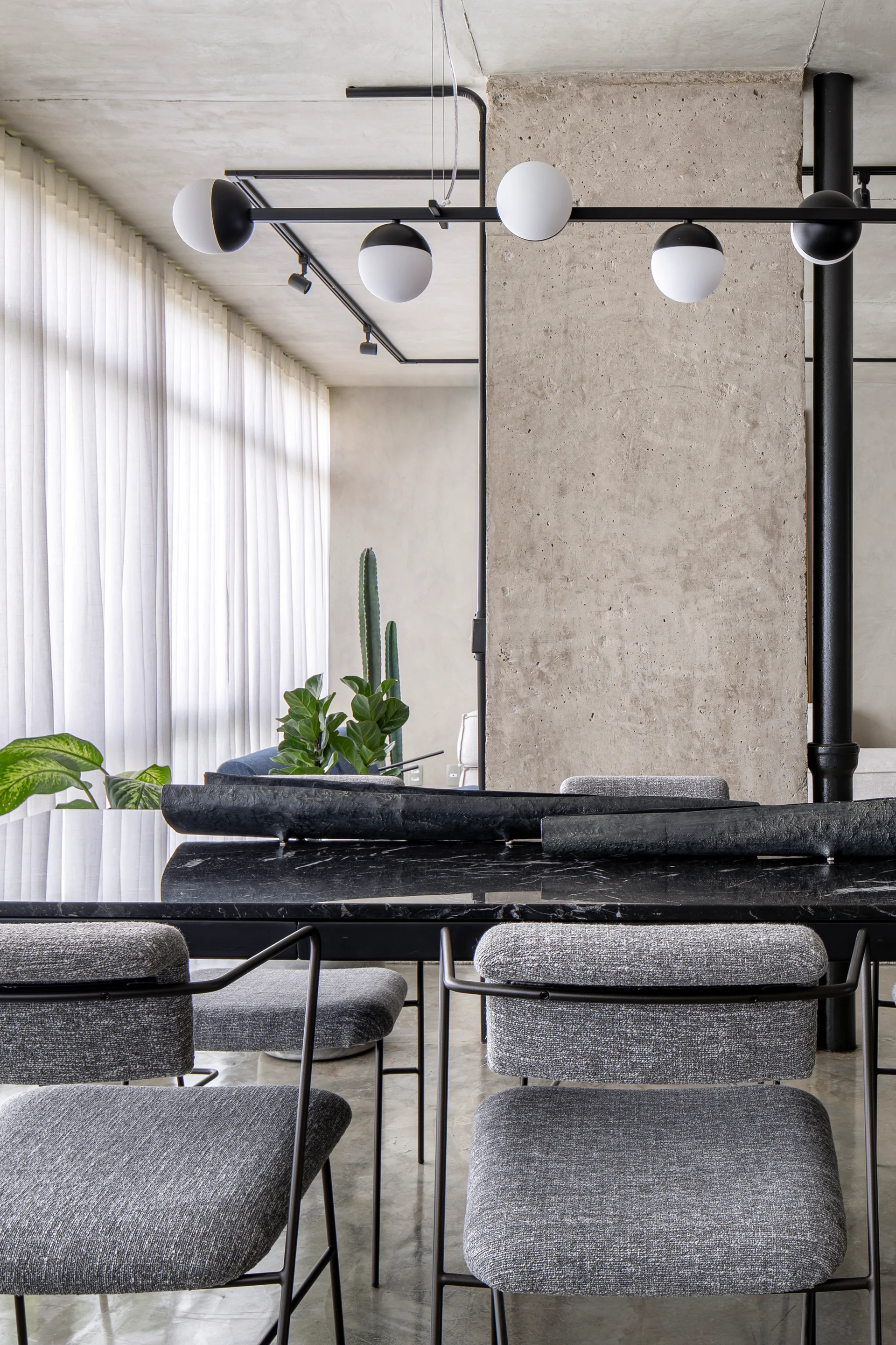 A modern dining room featuring a black marble table, gray upholstered chairs, and a raw concrete architectural column.