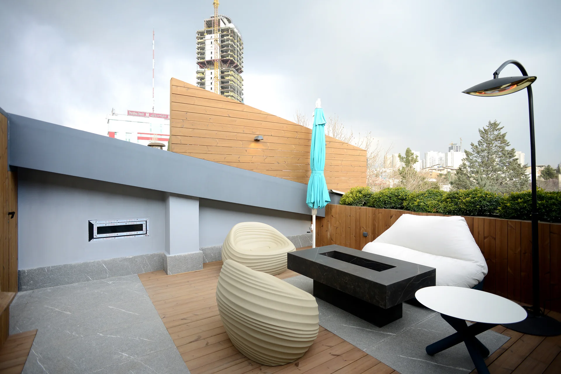 An outdoor terrace features a black rectangular fire pit, a white sofa, ribbed beige lounge chairs, and mixed wood and stone flooring.