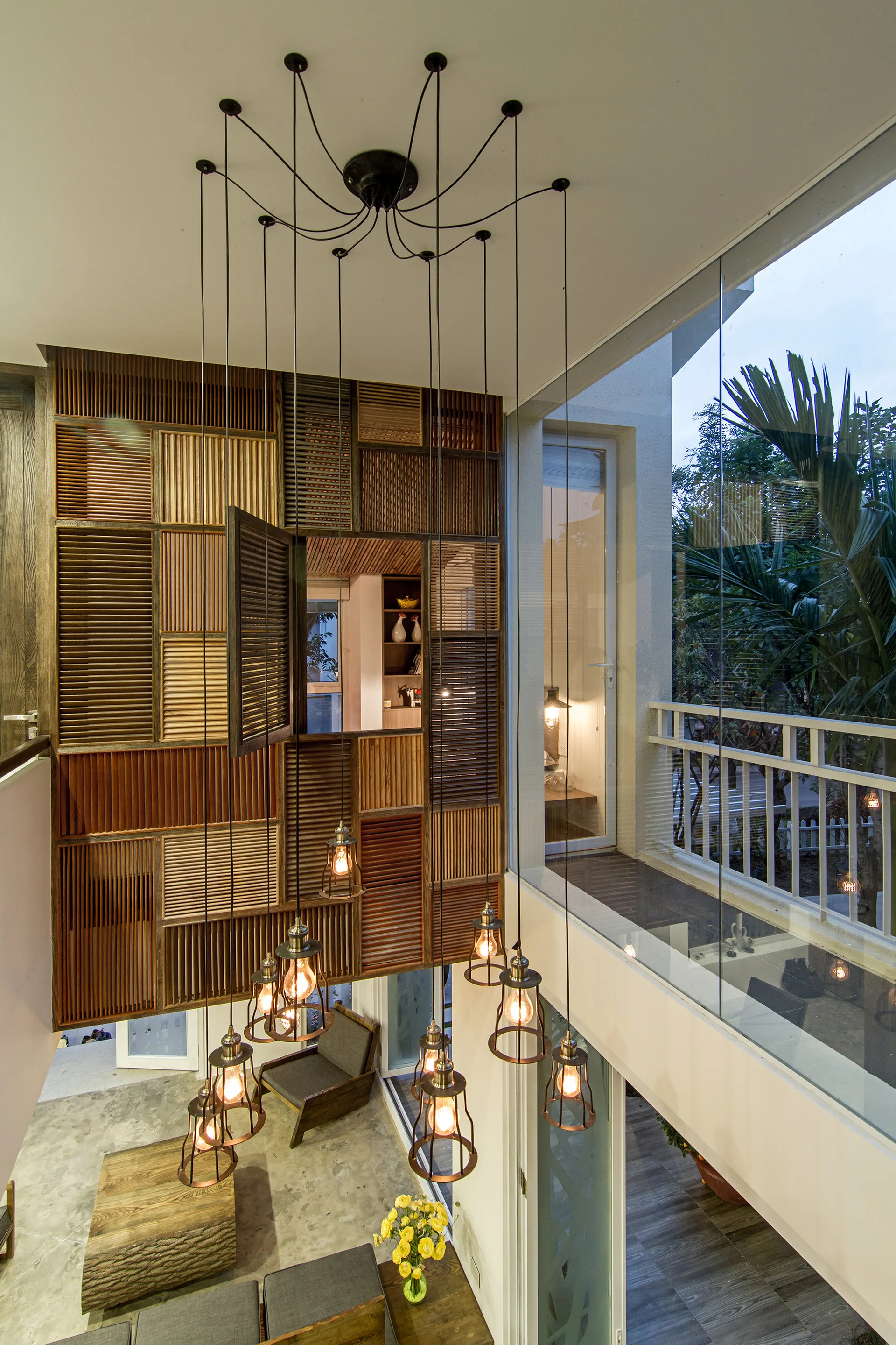A multi-level room featuring a grid of natural wood shutters on the wall and a multi-pendant industrial chandelier hanging from the ceiling.