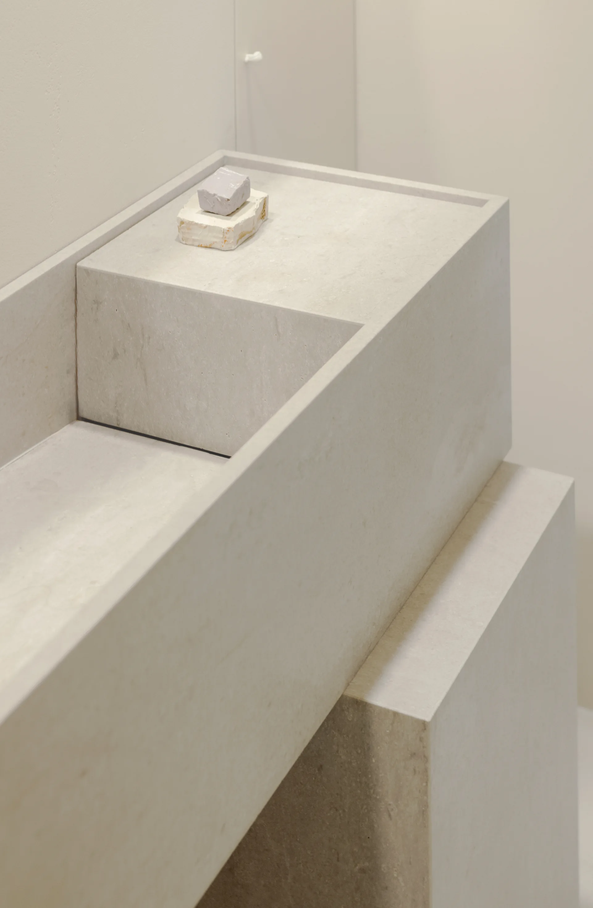 A close-up shot of a minimalist rectangular beige stone bathroom basin featuring an integrated soap shelf with a small bar of soap.