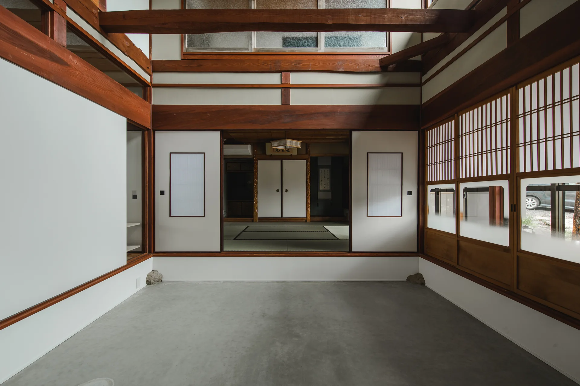 A traditional Japanese room features a smooth concrete floor in the foreground, sliding shoji screen doors, and high exposed wooden ceiling beams.