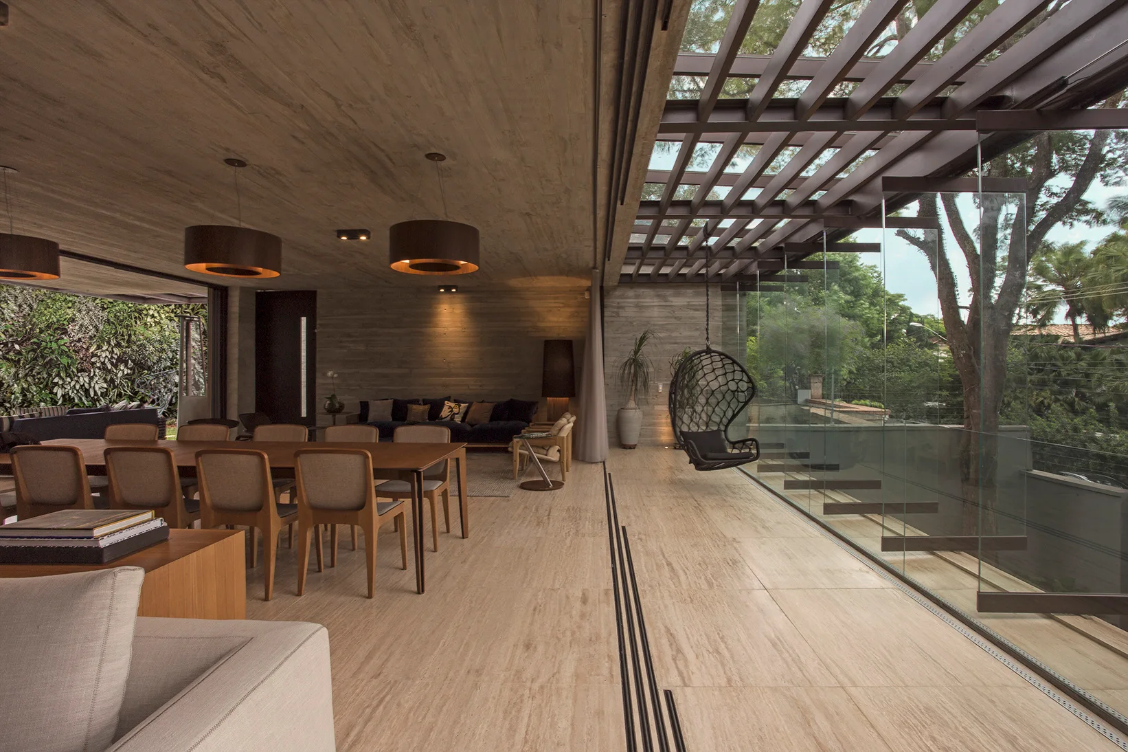 A modern open-plan dining and living space features a board-formed concrete ceiling, travertine tile flooring, and fully opened sliding glass walls.