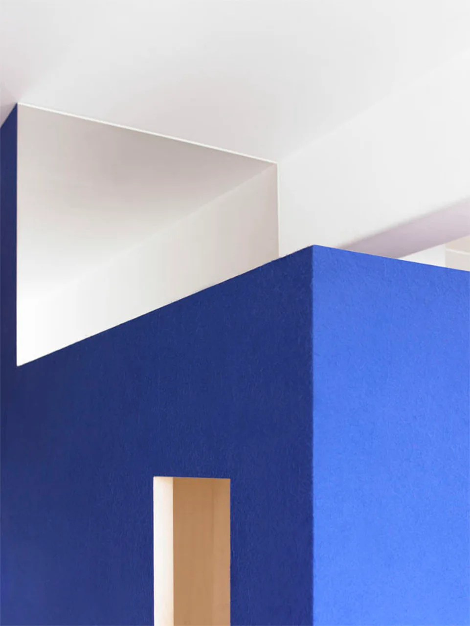 A close-up view of a matte cobalt blue interior wall with a geometric rectangular cutout against intersecting white ceiling planes.