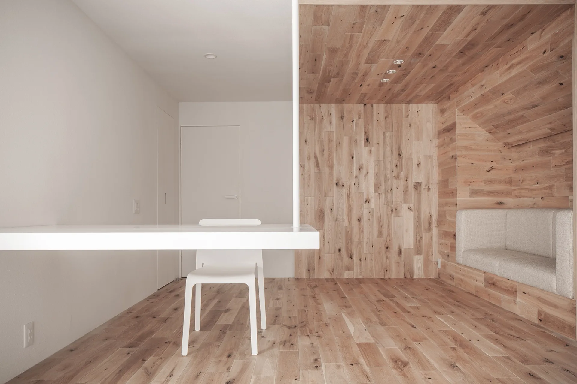 A minimalist room featuring a white wall-mounted desk and chair next to a fully wood-clad alcove with a built-in cushioned bench.