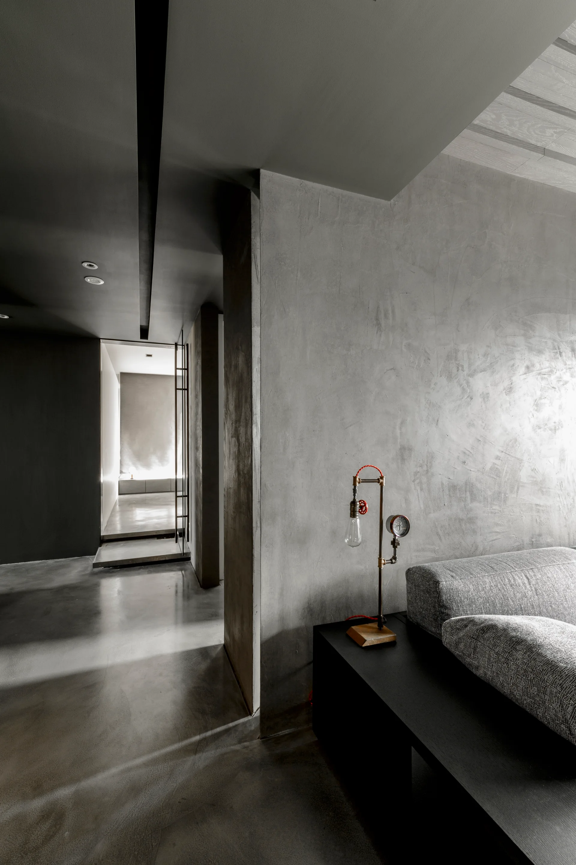 A gray minimalist living room showing a textured plaster wall, a gray sofa, and a custom industrial pipe lamp on a black console table.