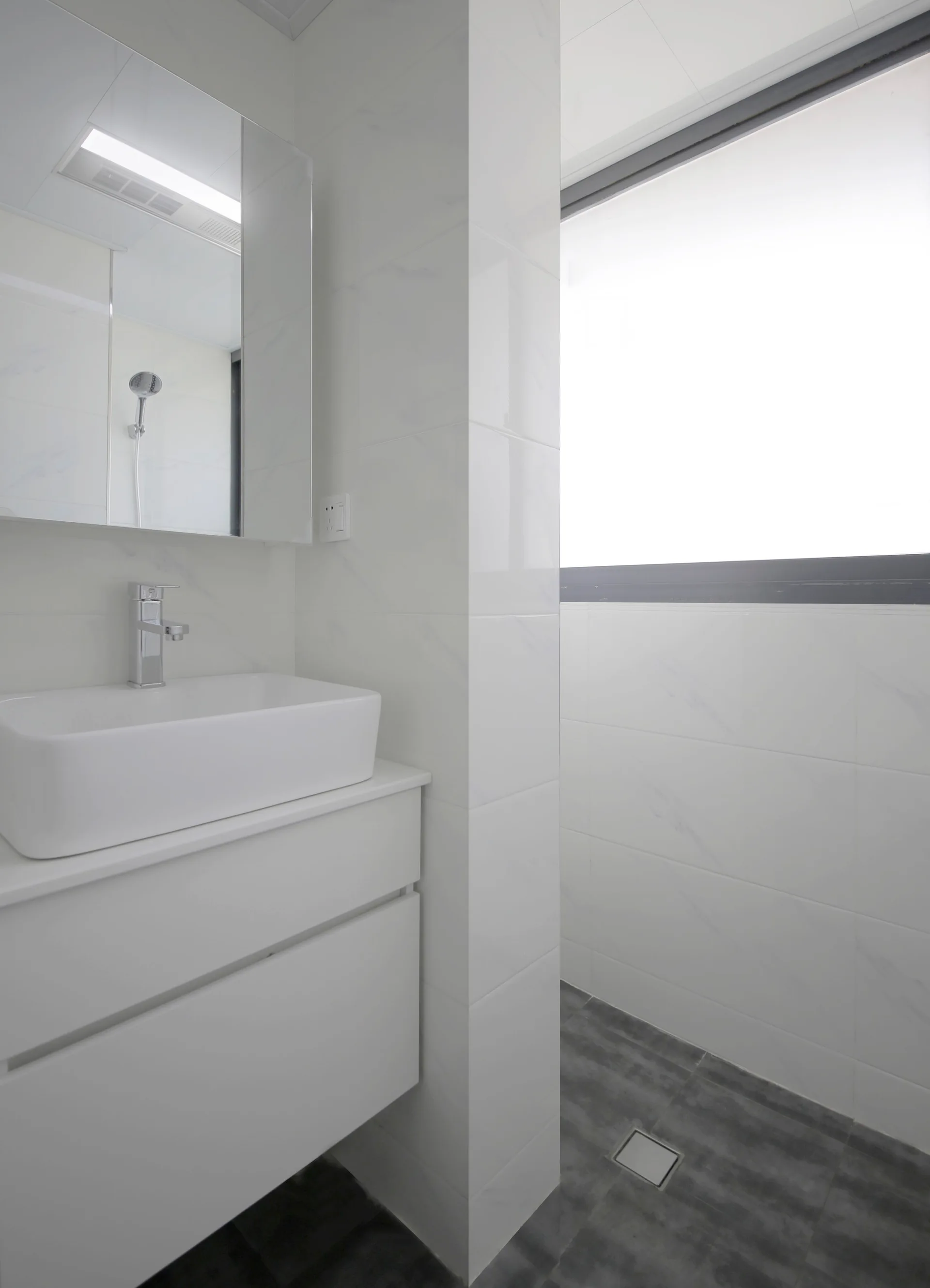 A minimalist bathroom features a white floating vanity with a rectangular countertop sink, glossy marble-look wall tiles, and grey tiled floors.